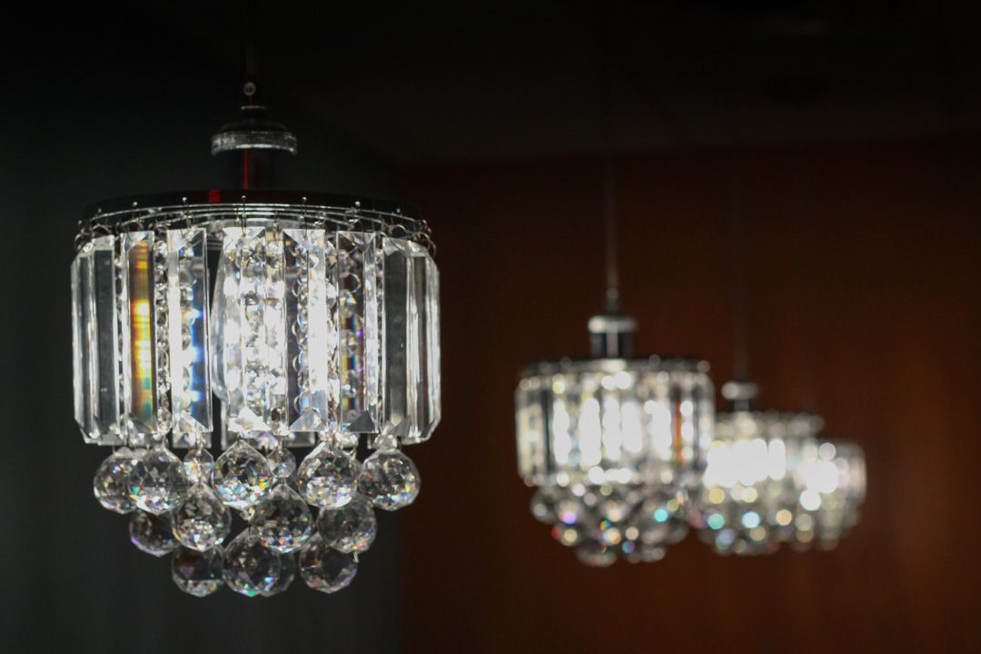 A row of three illuminated crystal chandelier-style pendant lights suspended against a dark, warm-toned background.