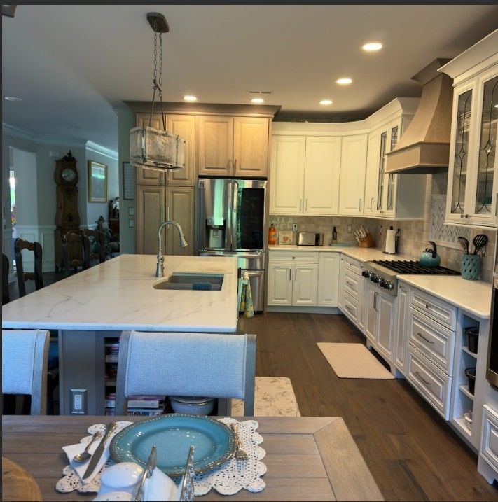 Modern kitchen with white cabinets, a large island with marble countertops, stainless steel appliances, and wood floors.