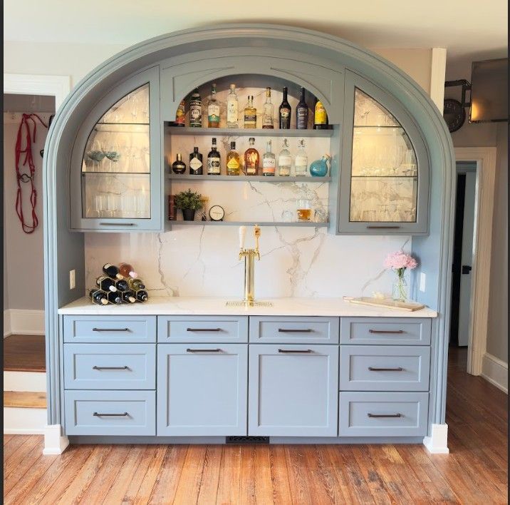 A built-in gray home bar with an arched display, white marble backsplash, gold beer tap, and matching storage cabinets.
