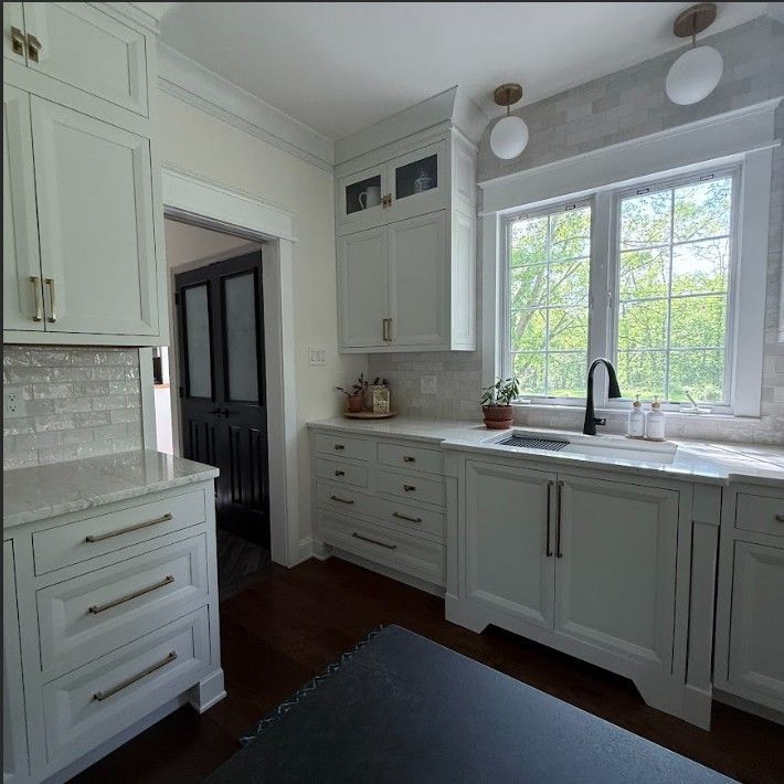 A bright kitchen featuring white cabinets, stone countertops, a large window over a sink, and dark wood flooring.