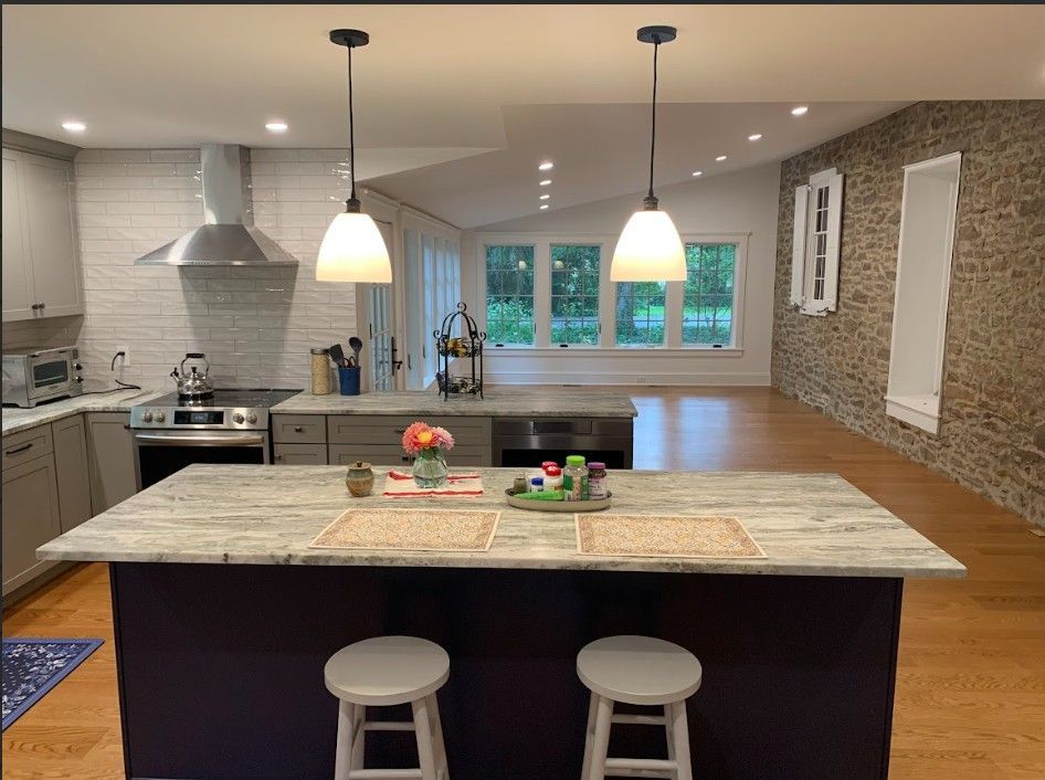 Modern kitchen with a purple island, white countertops, two pendant lights, and a textured stone feature wall.