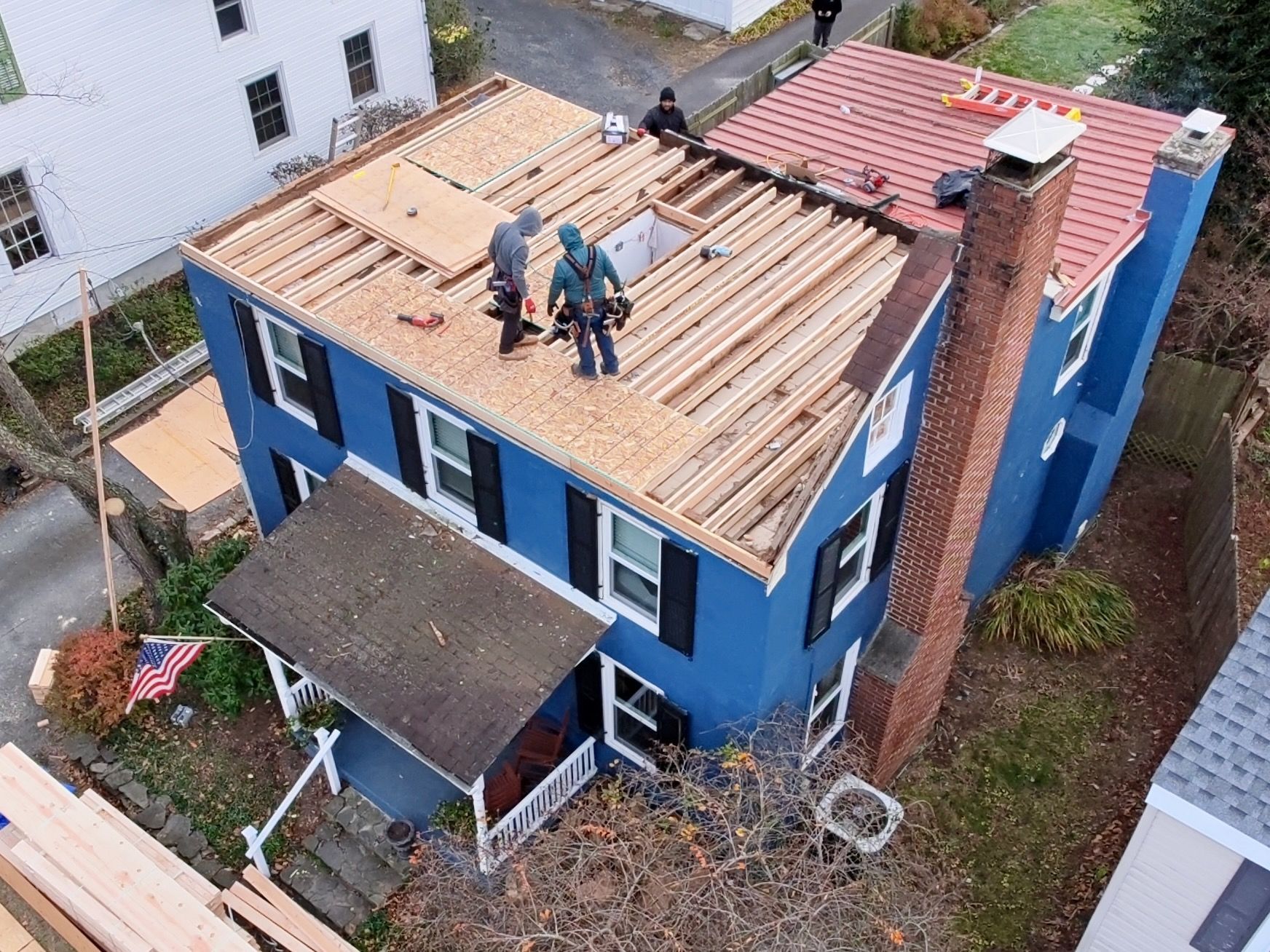 Aerial view of workers replacing the roof on a blue house; part of the roof is exposed framing and part is covered.