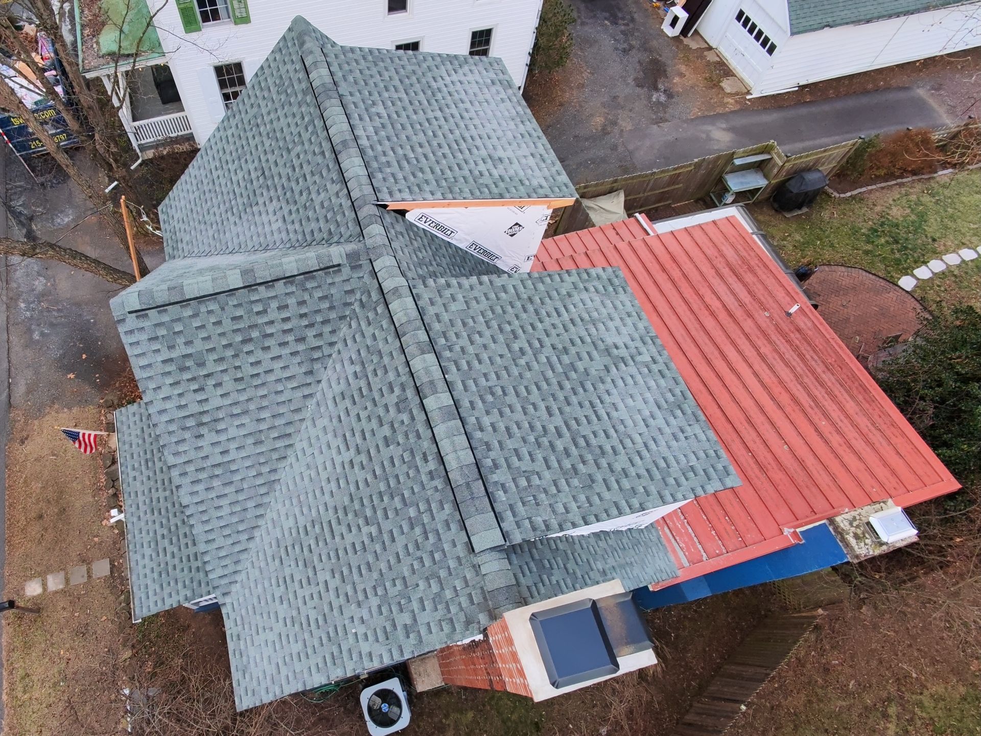 Aerial view of a home roof with green asphalt shingles on one section and red metal roofing on another.