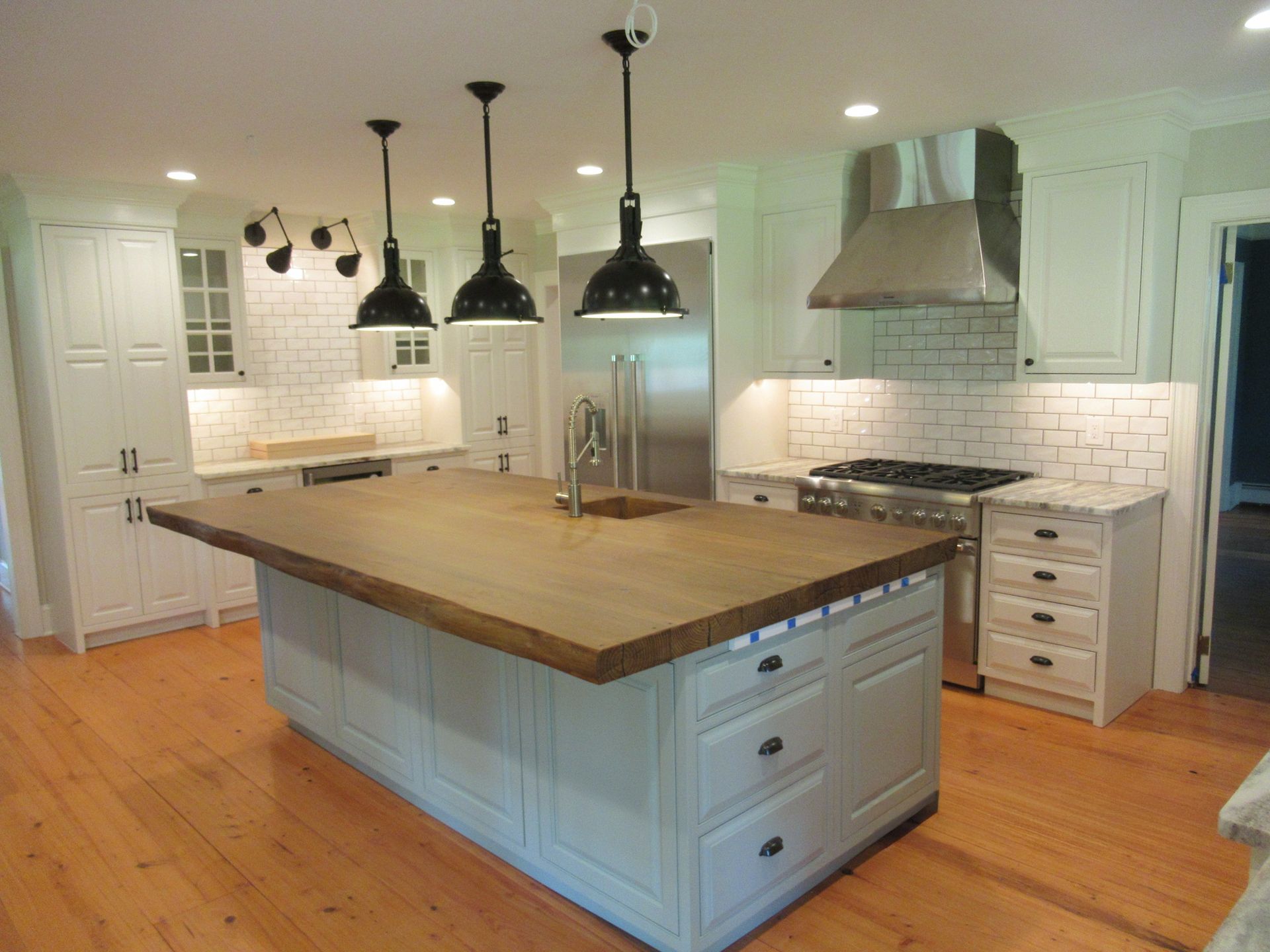 A brightly lit kitchen with a large wooden-topped island, white cabinets, stainless steel appliances, and wood flooring.