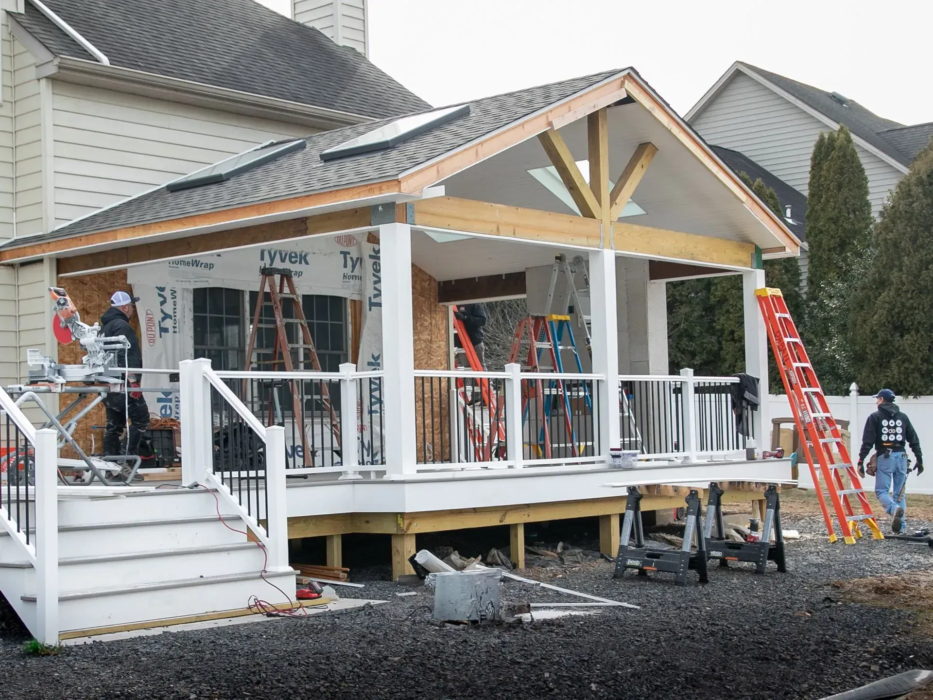 Construction of an outdoor covered deck with a white railing and wooden framing, tools scattered around.