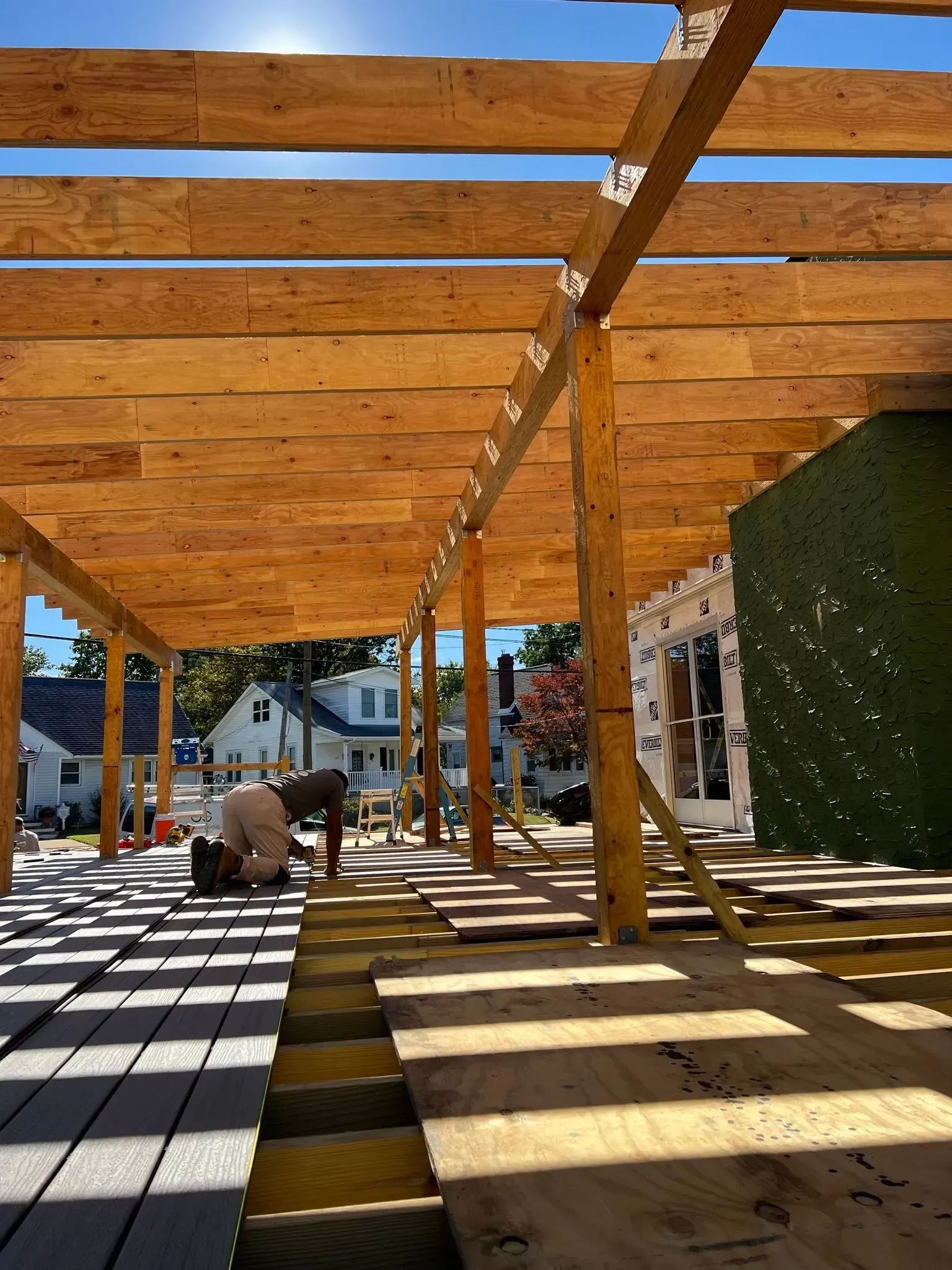 Construction site: worker on wooden deck, building frame, blue sky, sunlight.