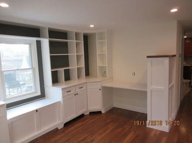 Bright white built-in shelving and cabinets in a small room with hardwood floor and large window