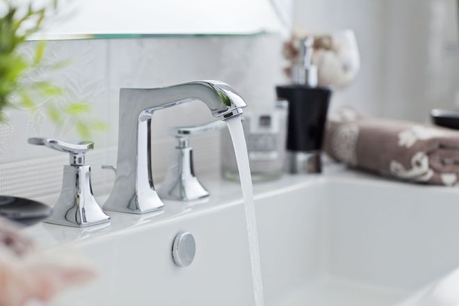 Chrome bathroom faucet with water running into a white sink.