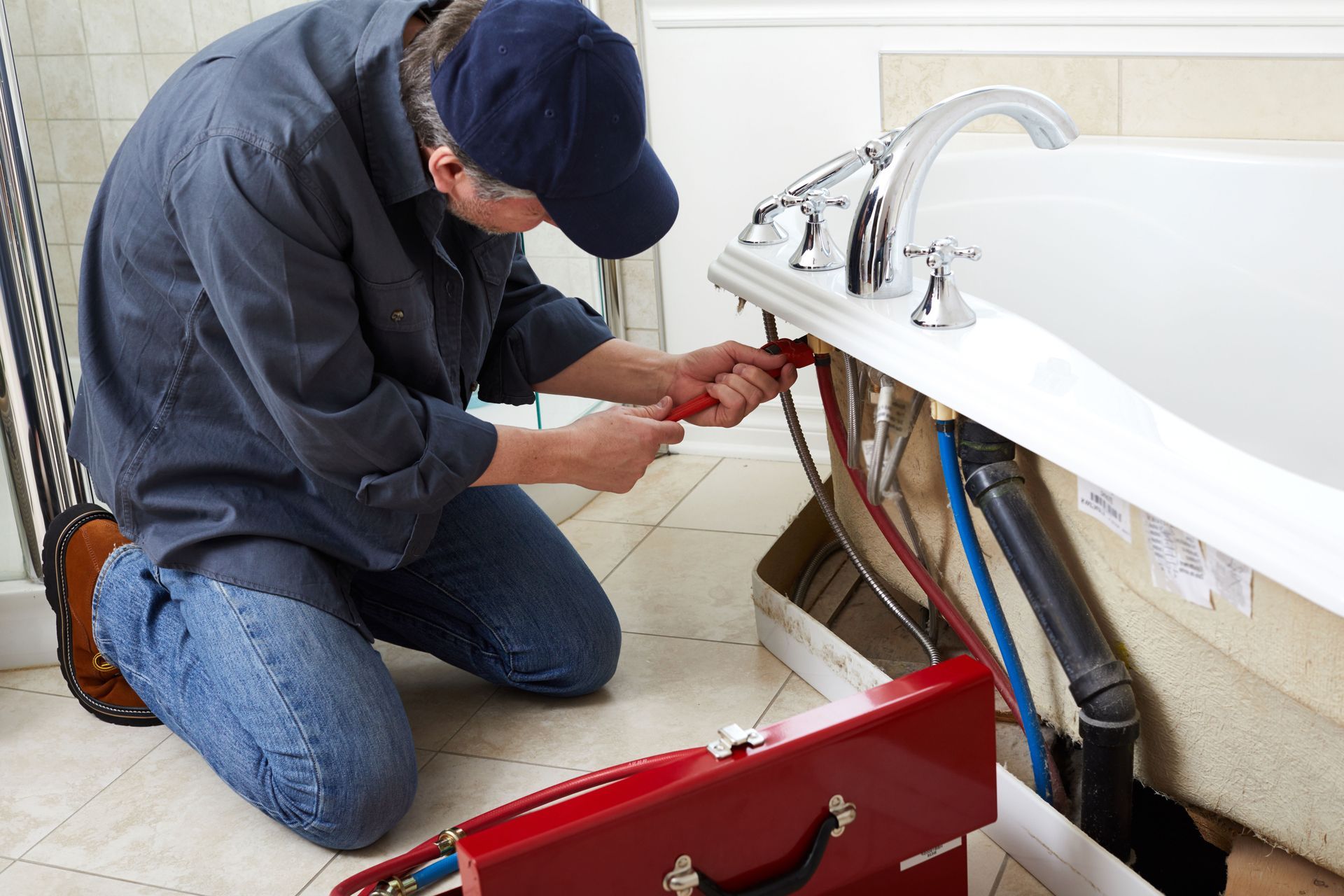 Plumber kneeling, working on bathtub plumbing with tools, in bathroom.