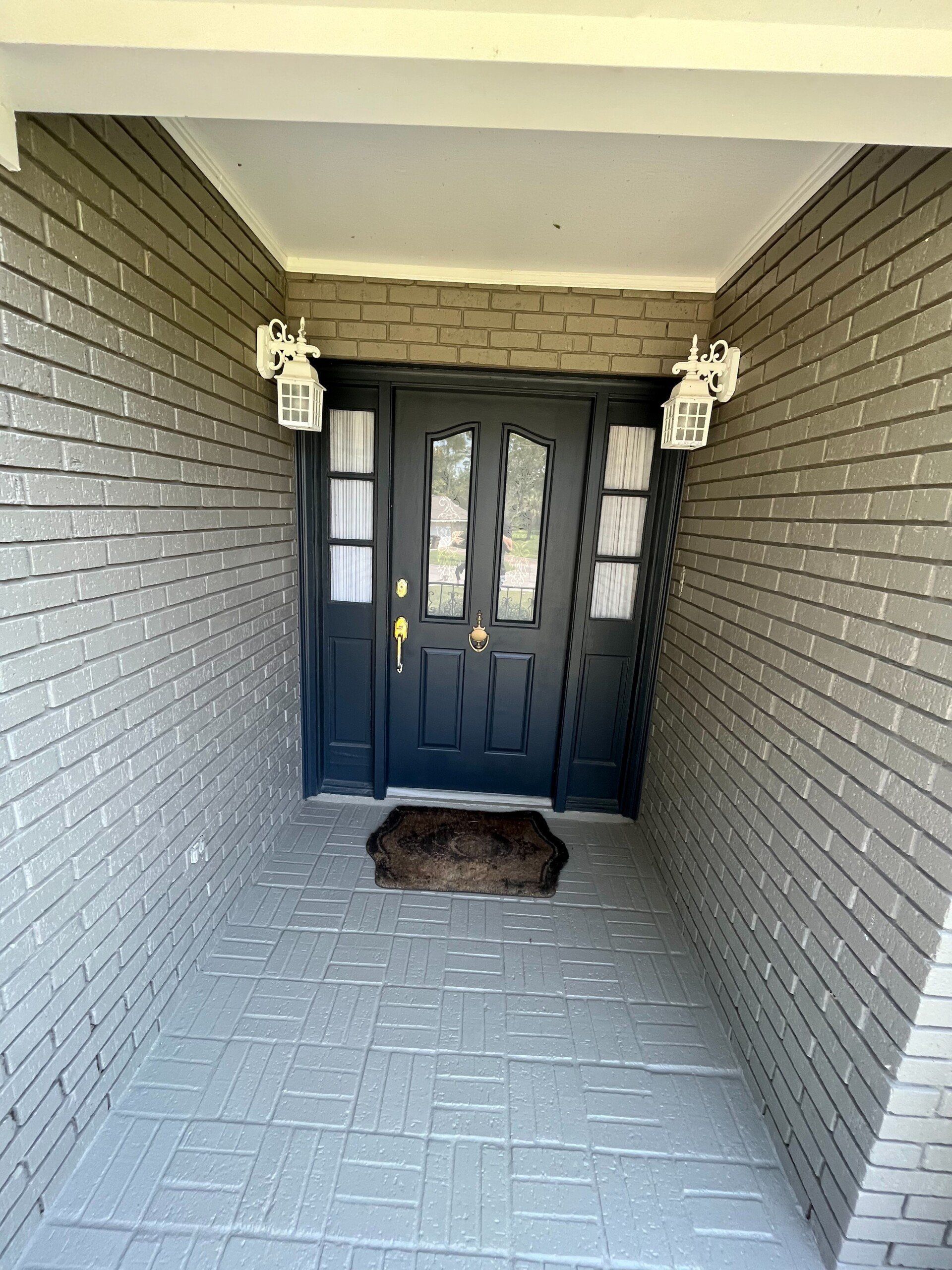 remodeled gray brick entrance with black door and white porch lamps