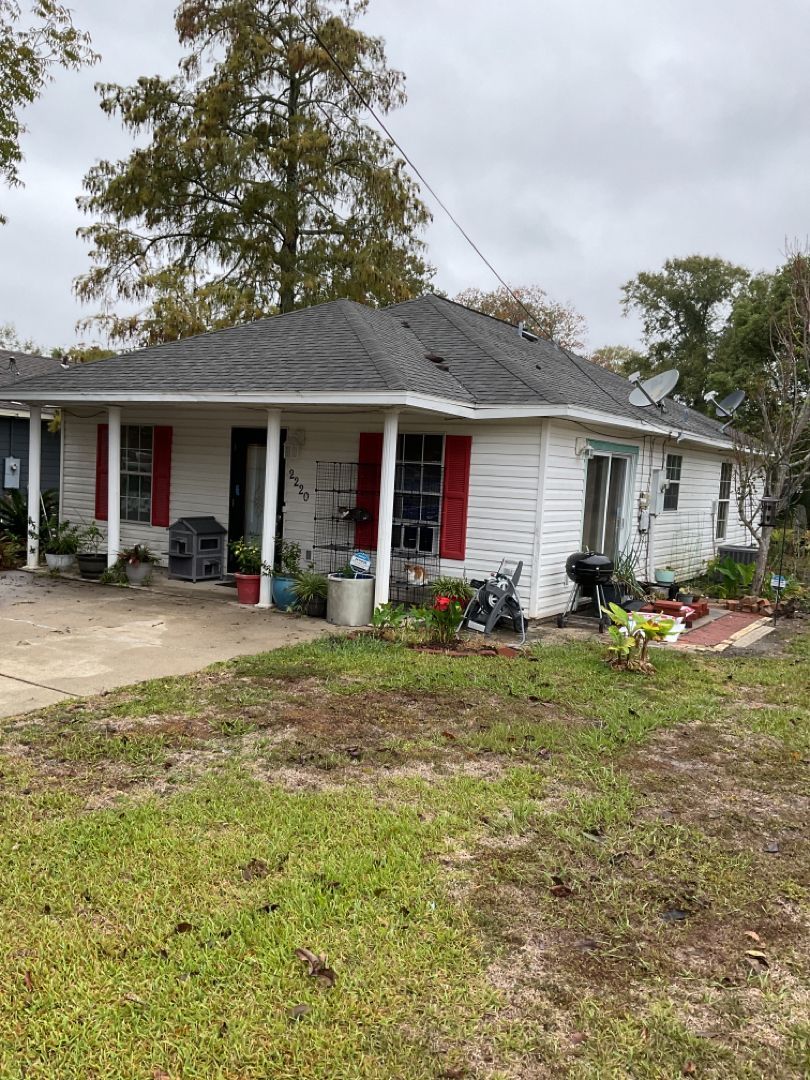 A white house with red shutters and a gray roof sits on top of a lush green field