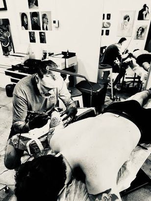 A man is getting a tattoo on another man 's back.