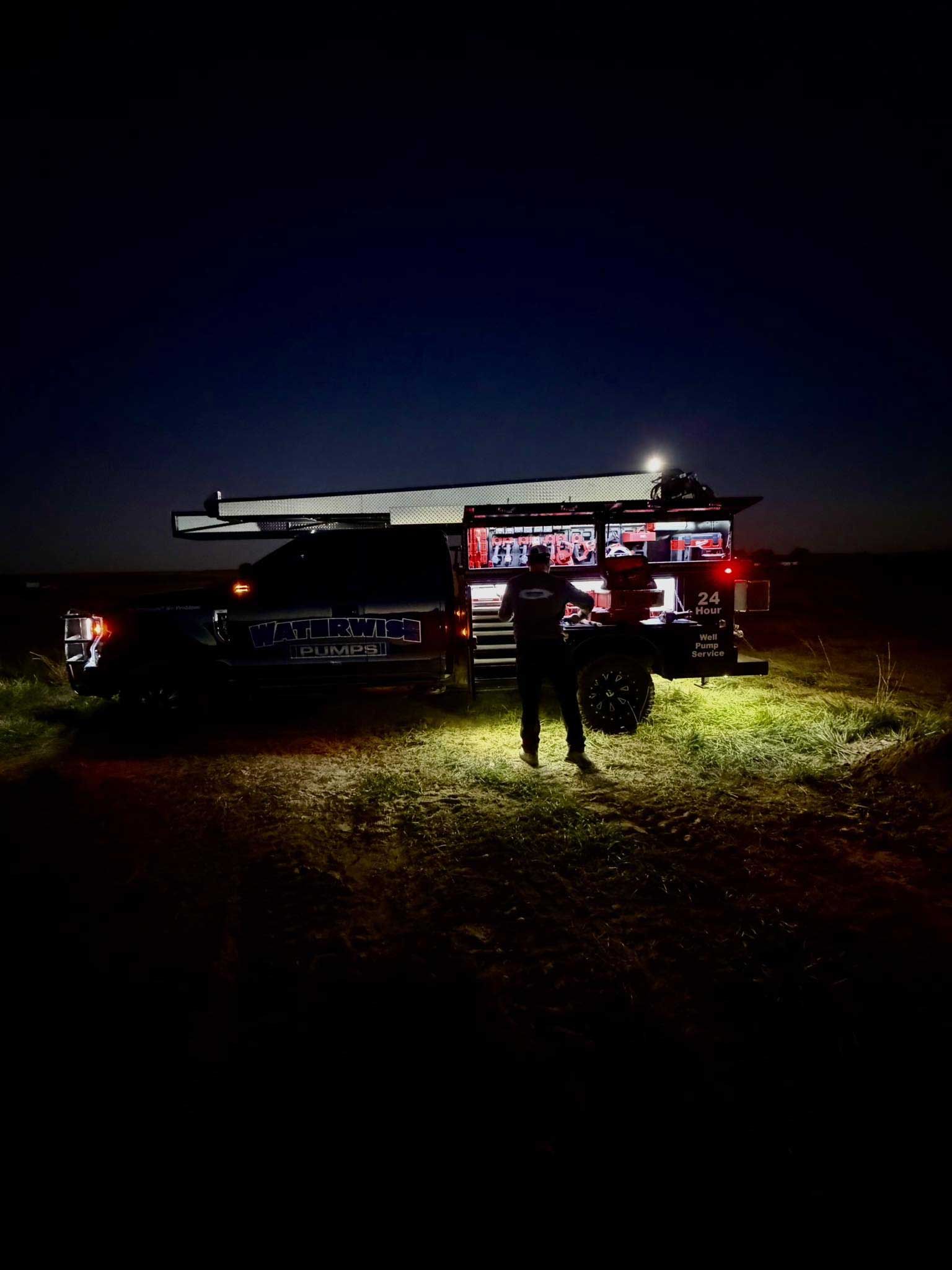 Person stands near a truck with lights on at night.