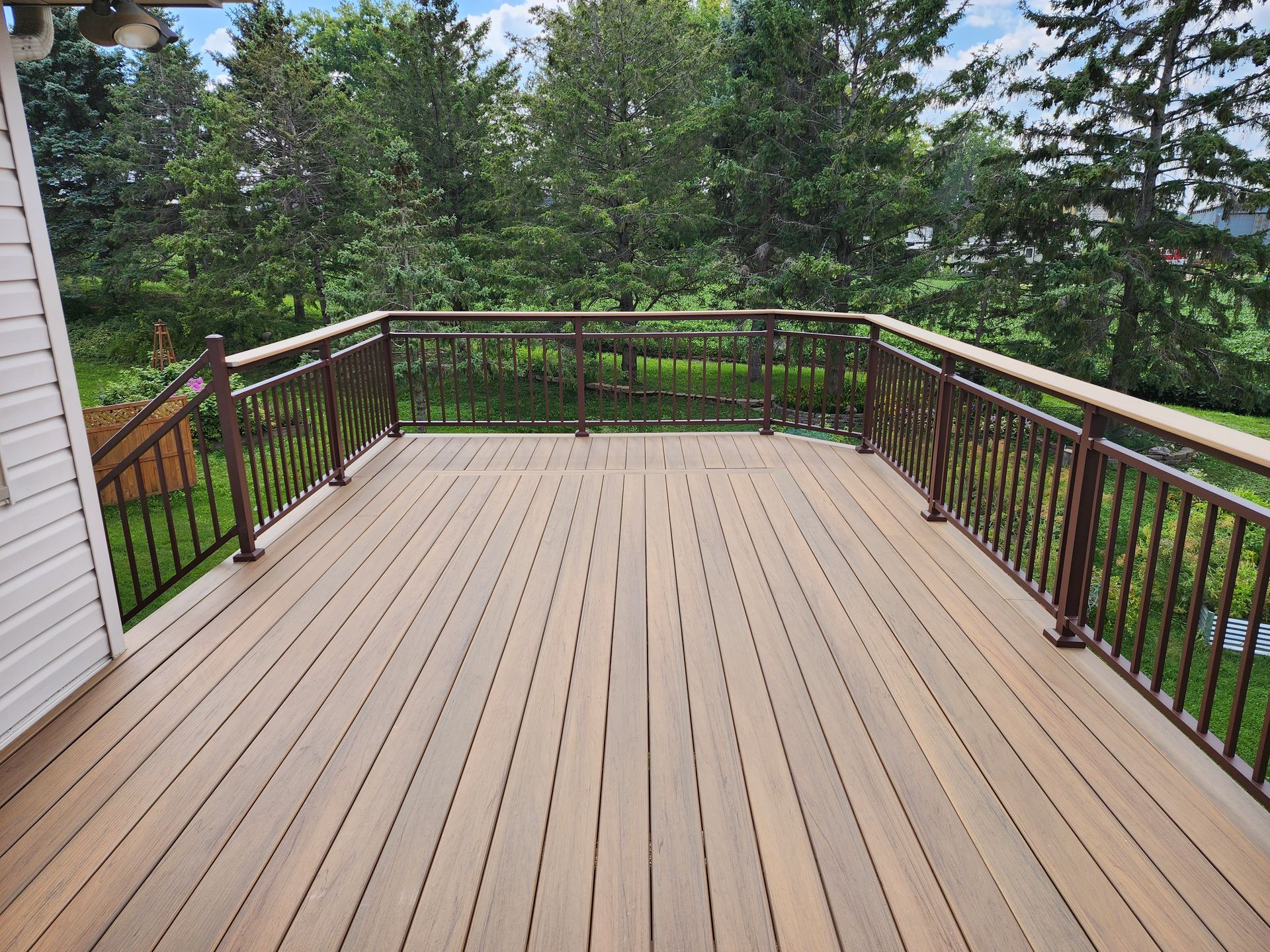 A large wooden deck with a metal railing and trees in the background.