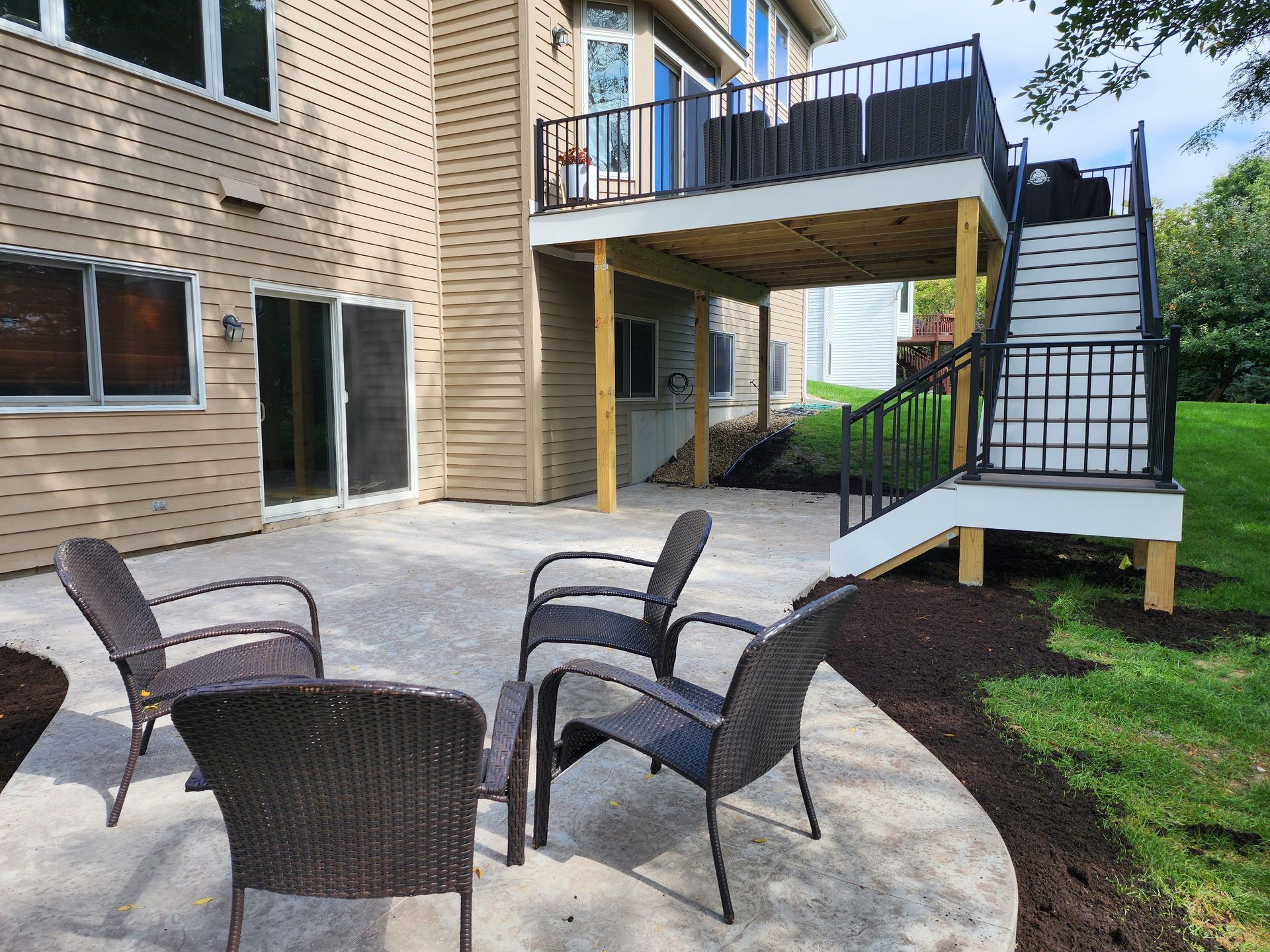 A patio with chairs and a table in front of a house with a deck.