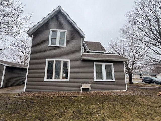 A house with a gray siding and white windows is sitting on top of a lush green field.