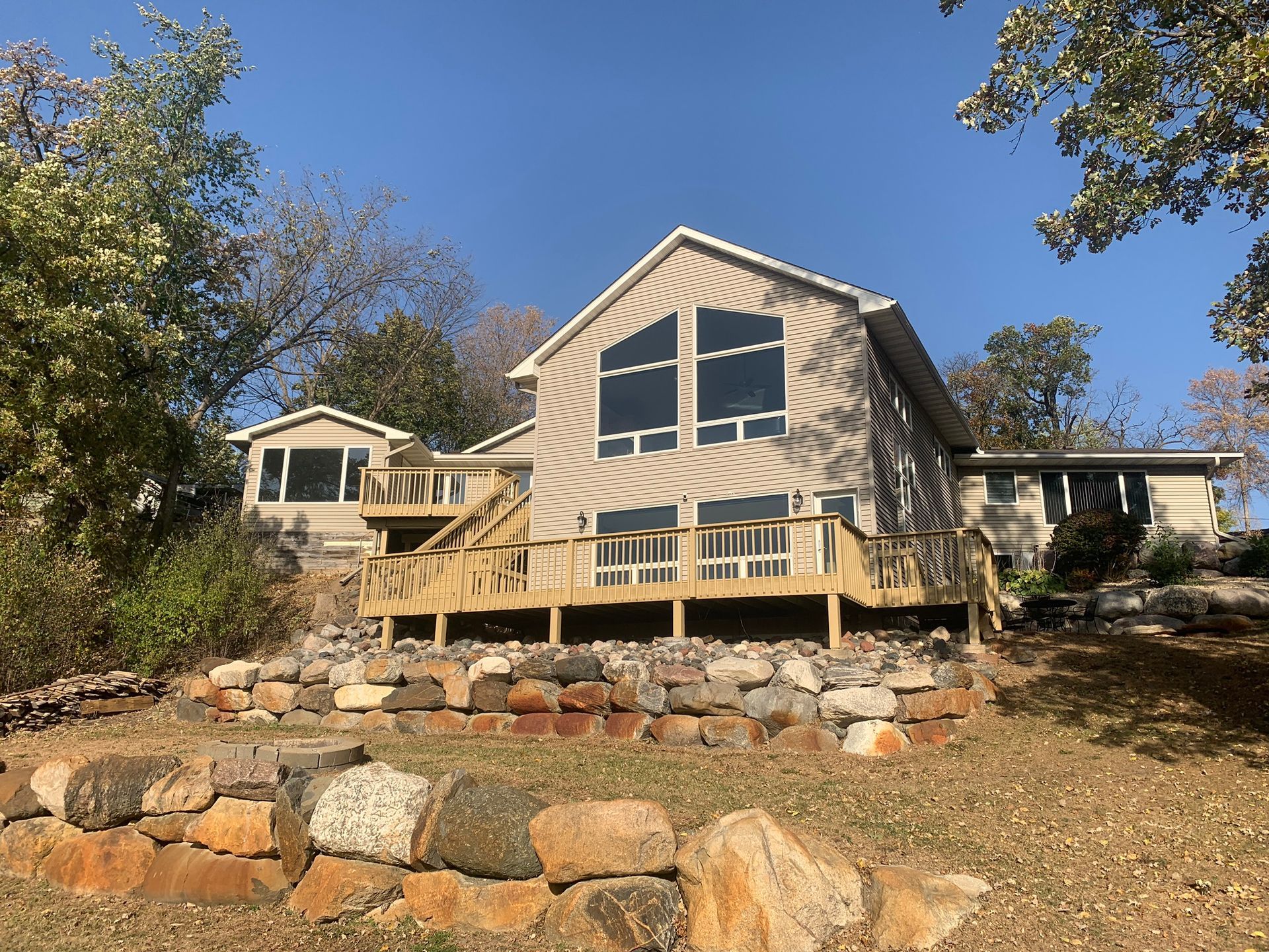 A large house with a large deck is sitting on top of a rocky hill.