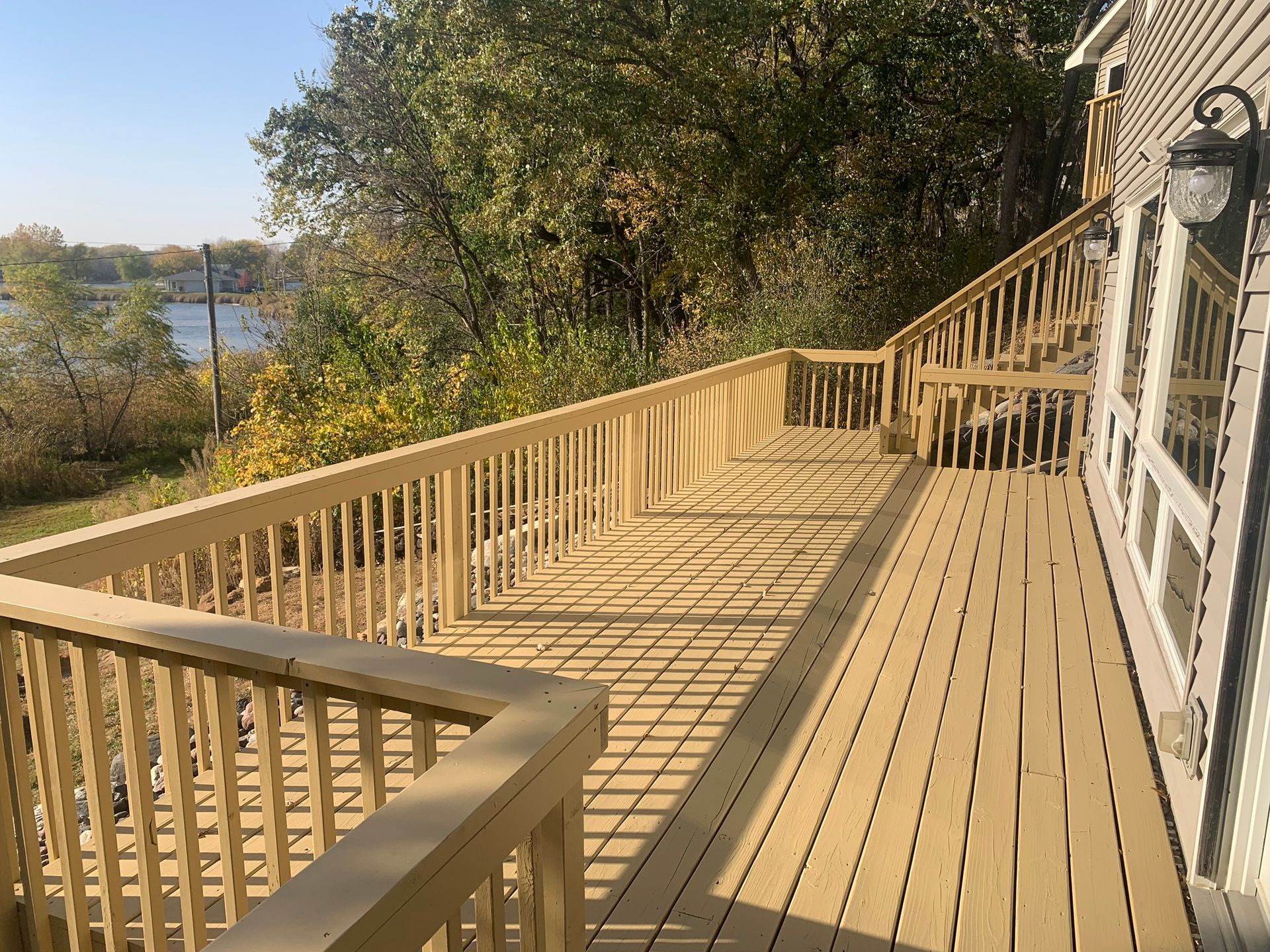 A large wooden deck with a railing and a view of a lake.