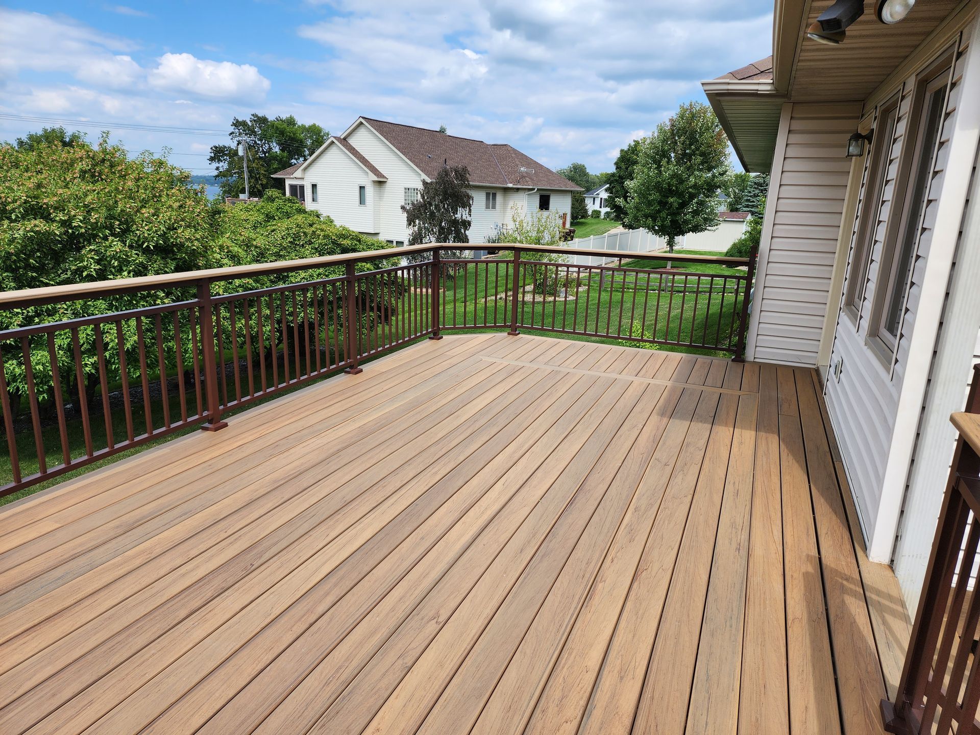 A large wooden deck with a railing in front of a house.