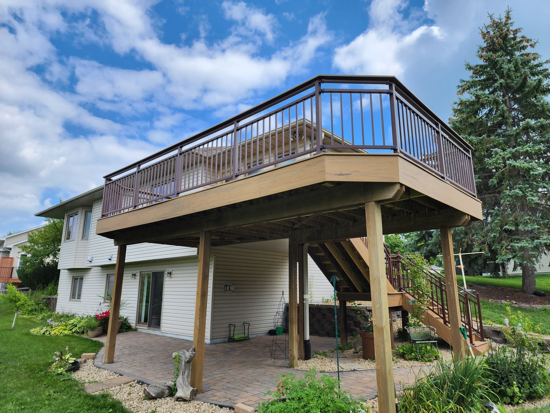 A large wooden deck with stairs leading up to it is in the backyard of a house.