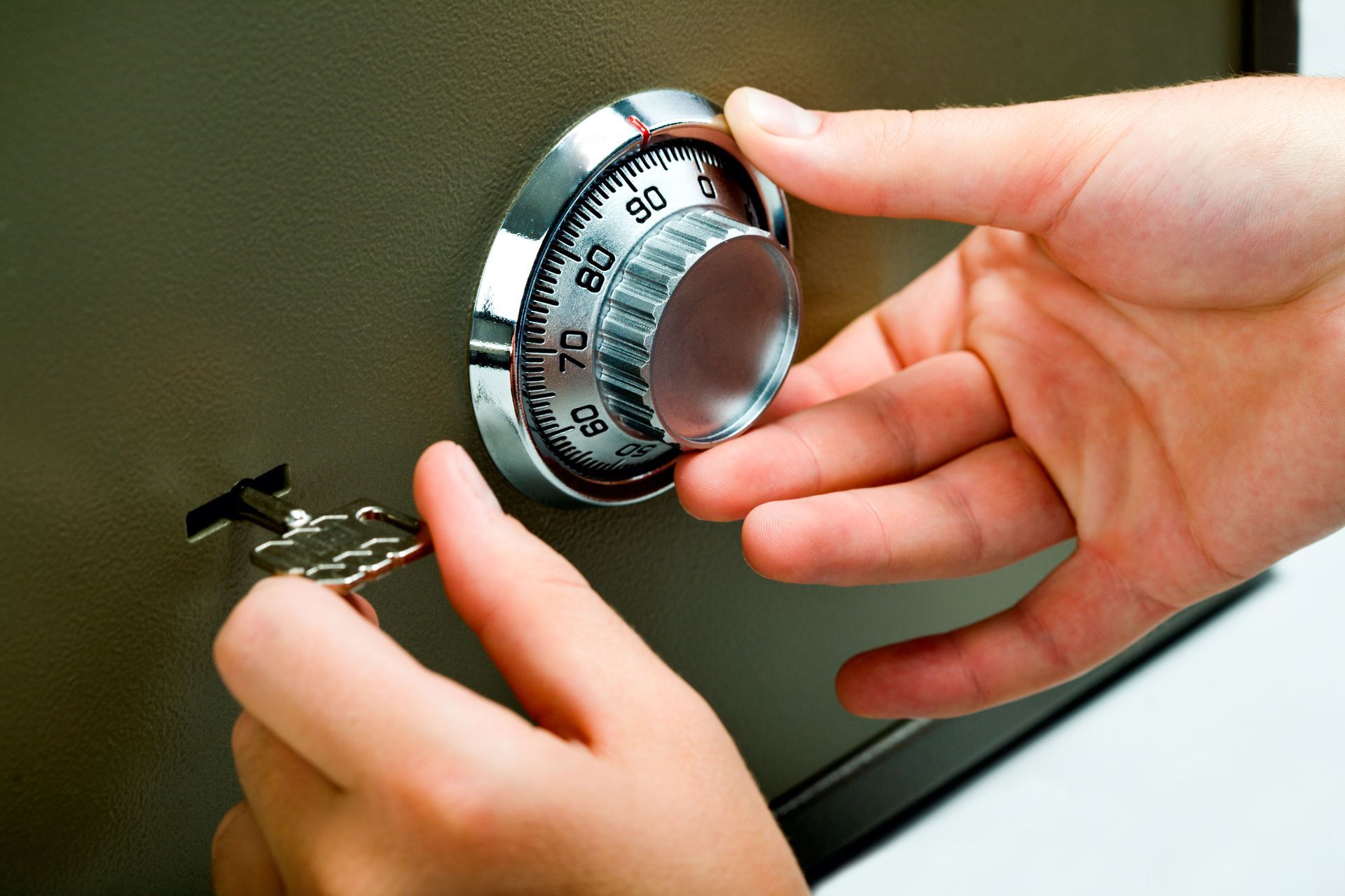 Hands turning a silver combination lock on a green safe or locker