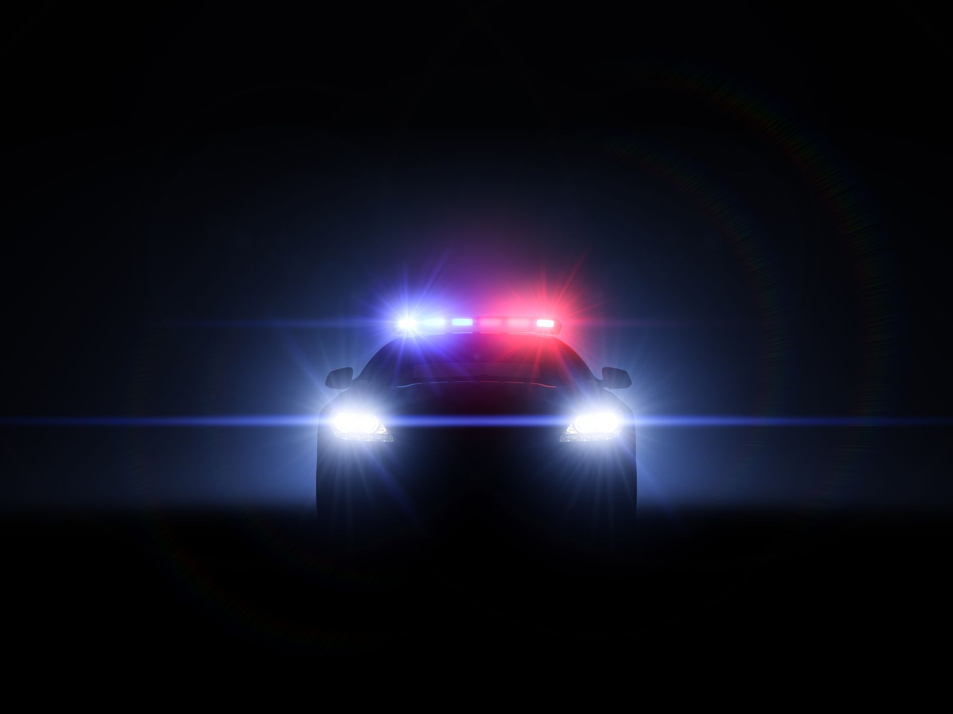Police car at night with red and blue flashing lights against a dark background