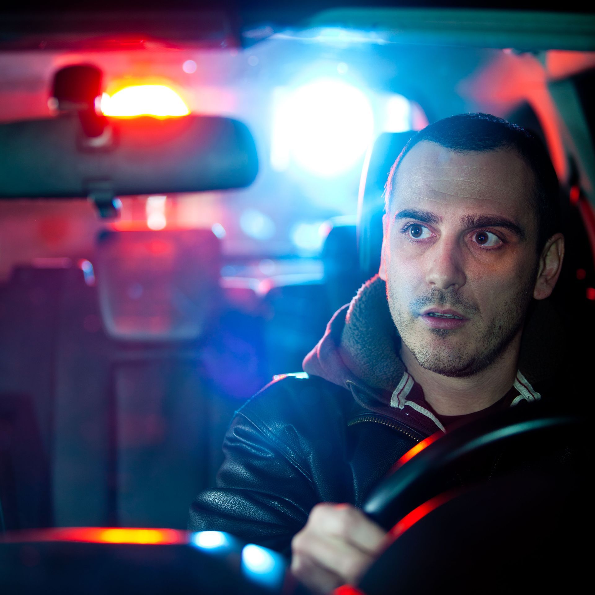 Man driving a car at night with red and blue police lights flashing behind him
