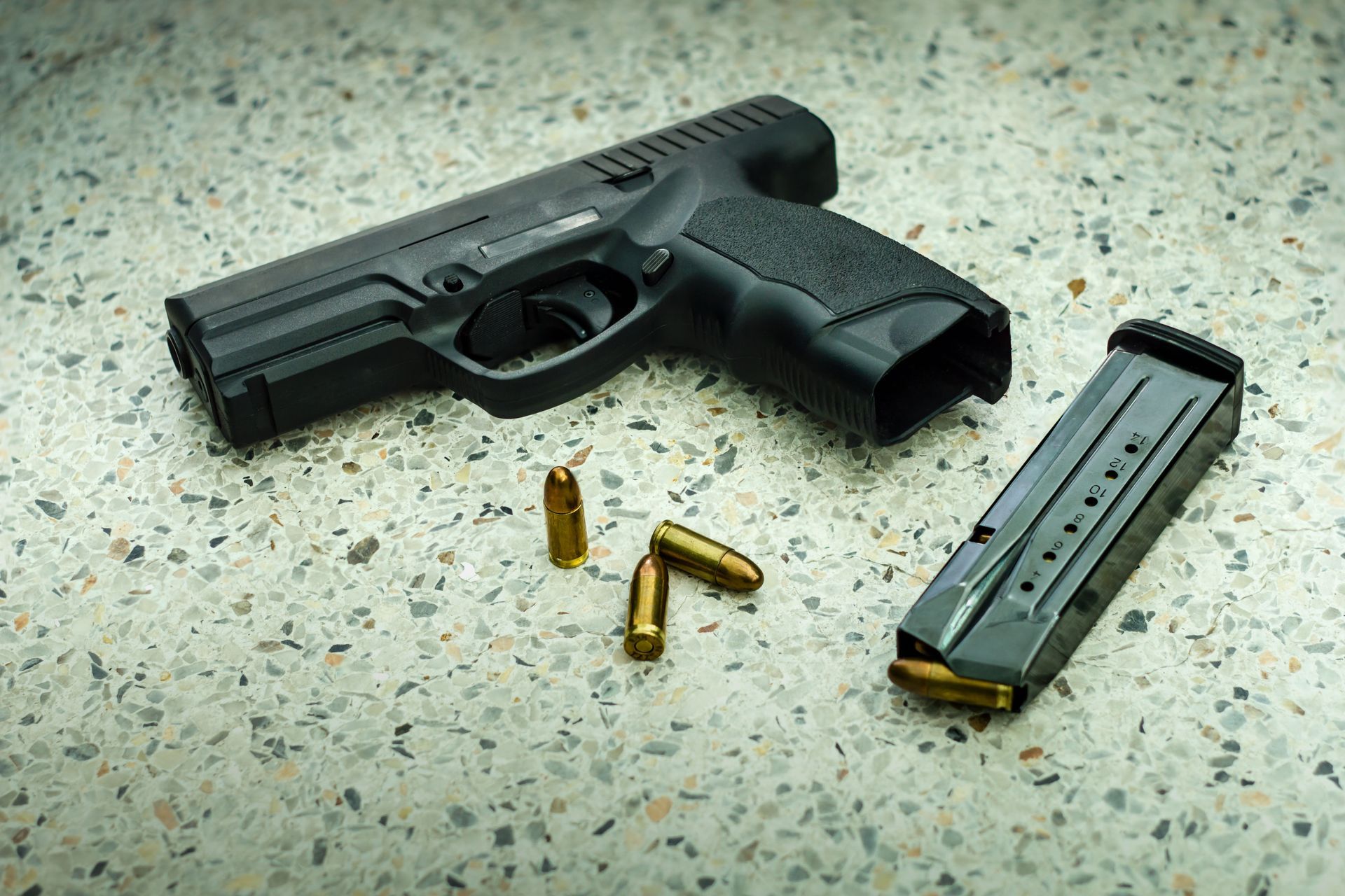 Black handgun with magazine and loose bullets on speckled floor