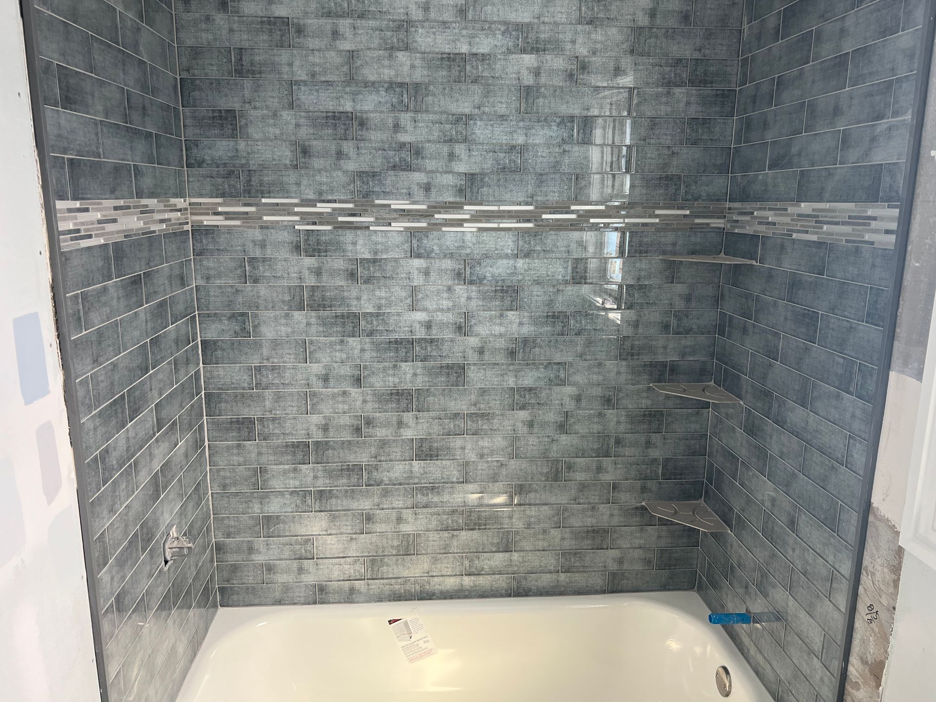 Bathtub alcove with gray brick-pattern tile and mosaic accent shelves.