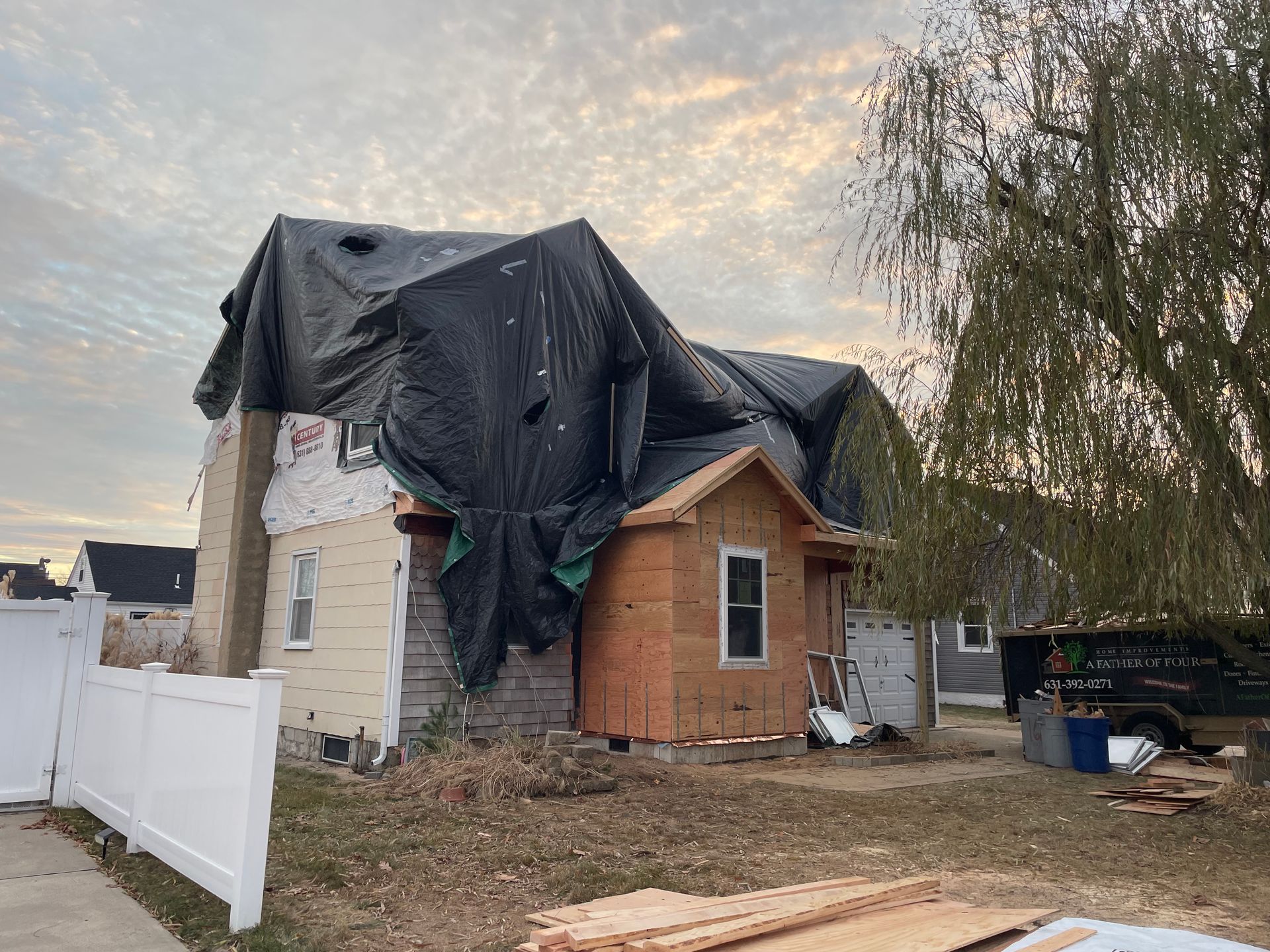 House with tarp covering damaged roof; exterior construction underway.