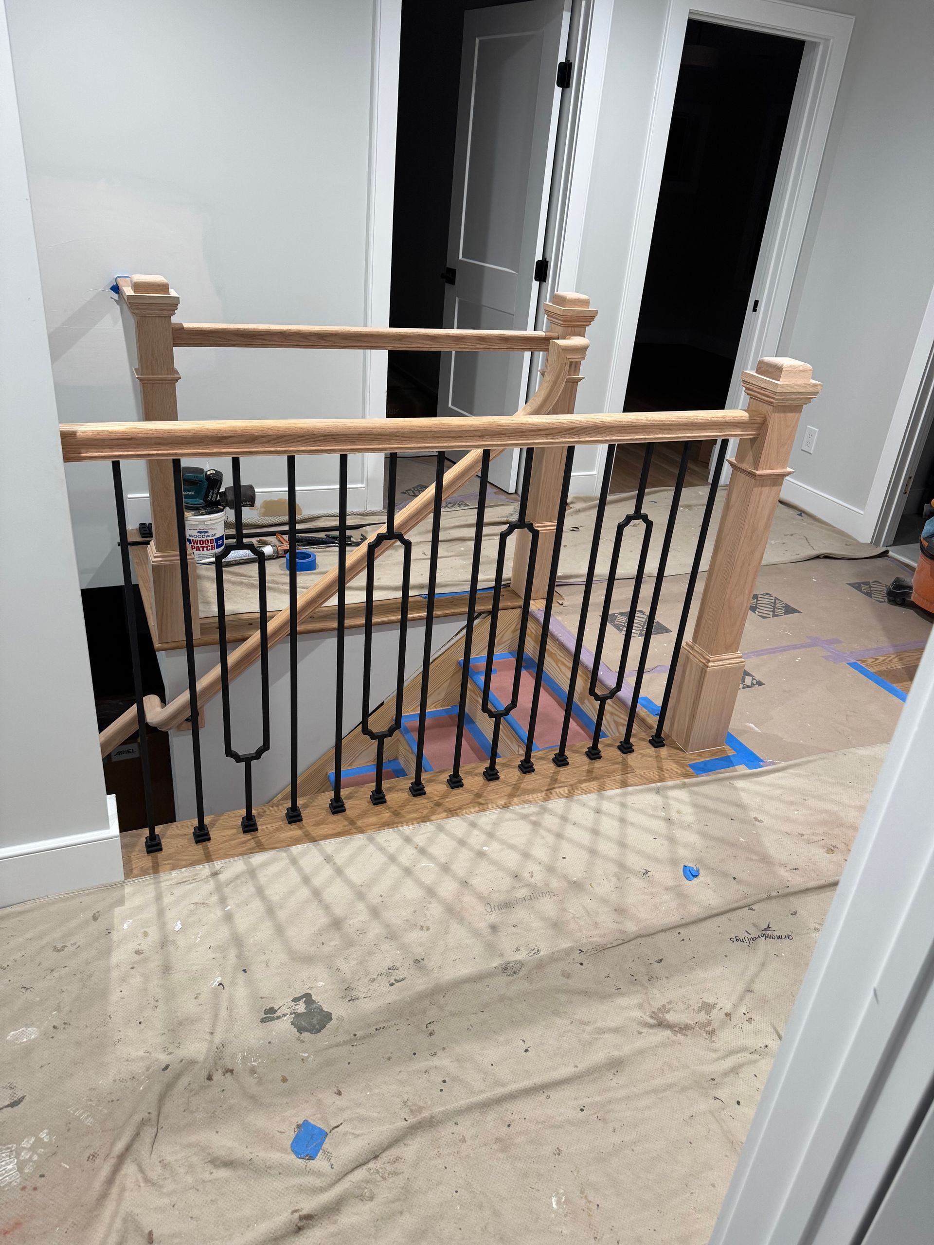 Newly installed staircase with black wrought iron spindles and light wood posts and handrails.