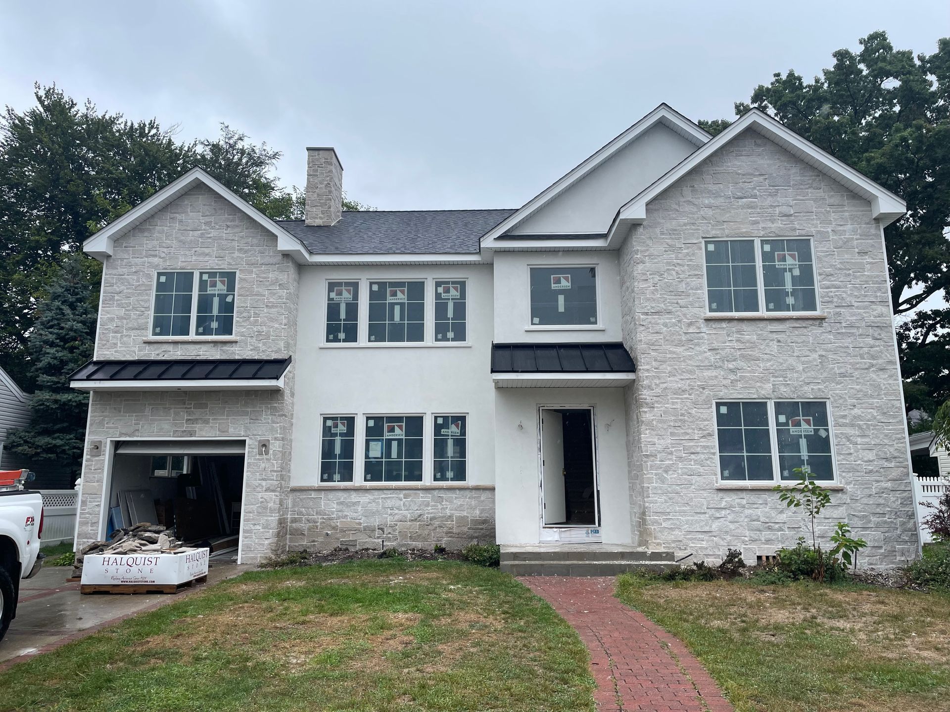 Two-story house under construction with light brick facade, white trim, and a black roof.