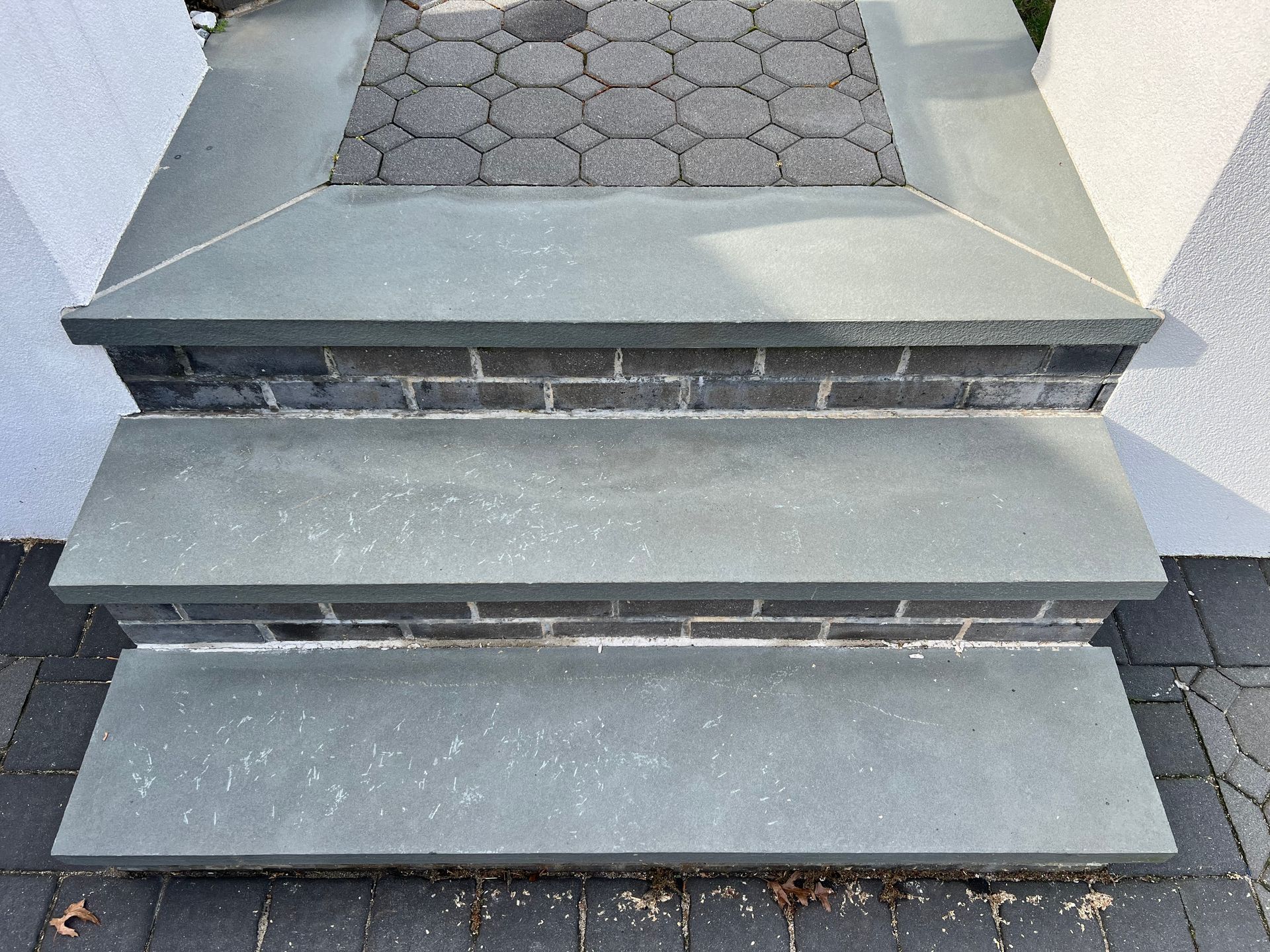 Three-step gray stone and brick outdoor staircase leading to a doorway, set against a cobblestone path.