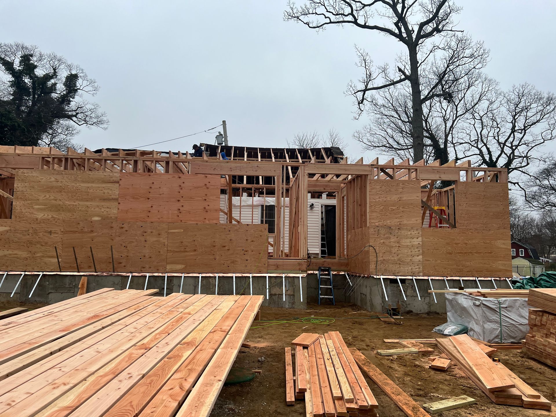 Construction site with a wooden house frame, building materials, and cloudy sky.