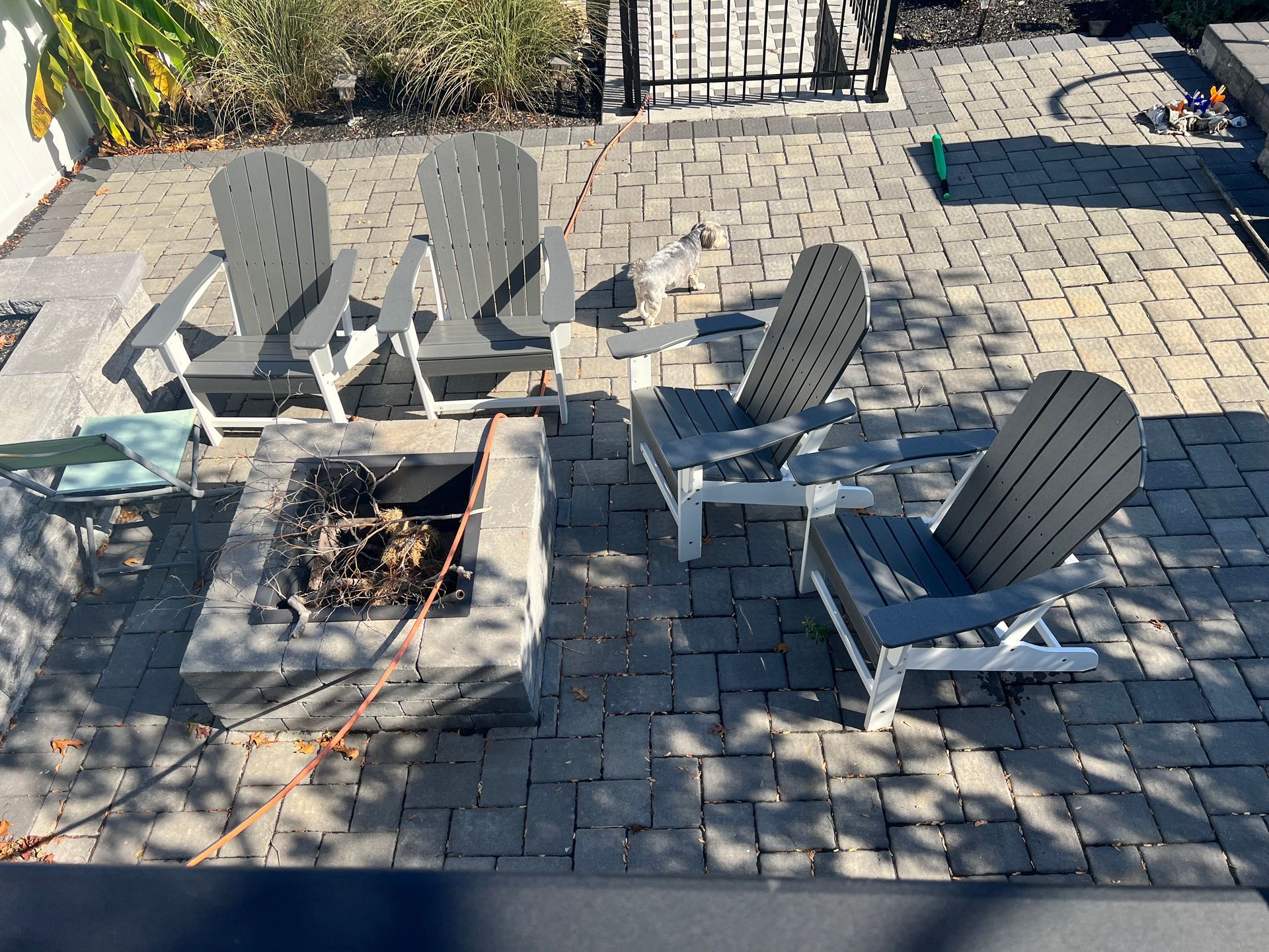 Four gray and white Adirondack chairs around a square stone fire pit on a brick patio.