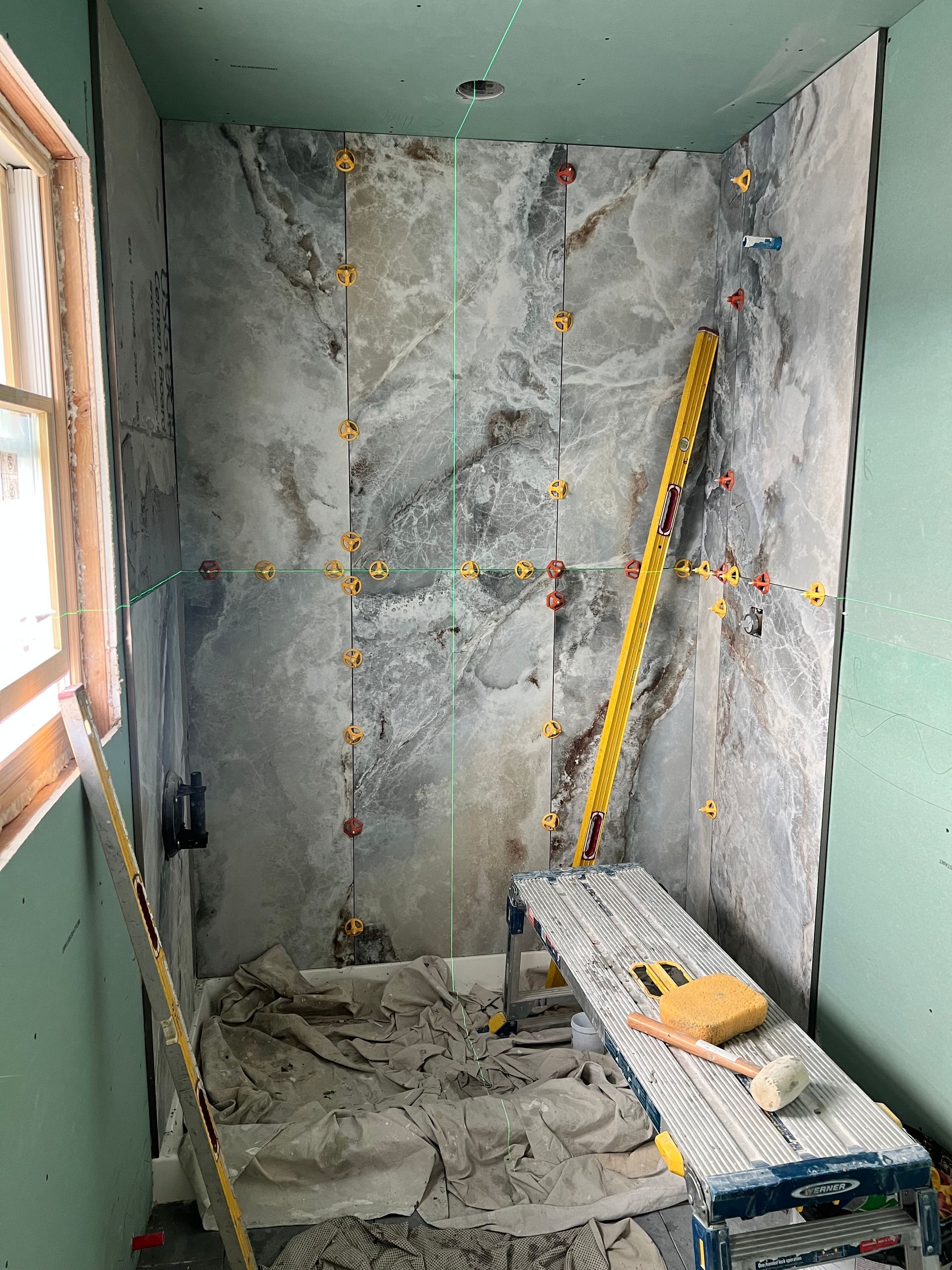 Shower stall under construction, with gray marble tiles, level, spacers, and construction materials visible.