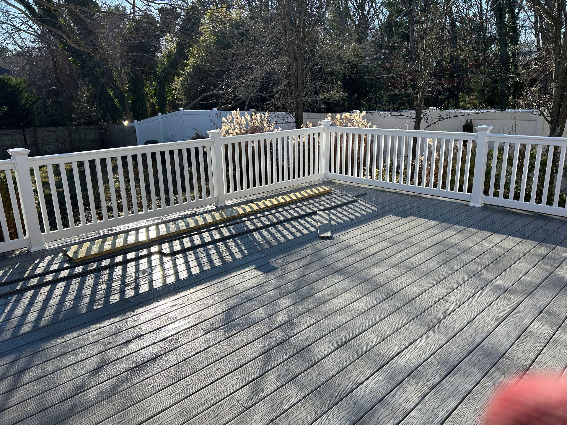 White-railed deck with gray flooring in a sunny backyard.