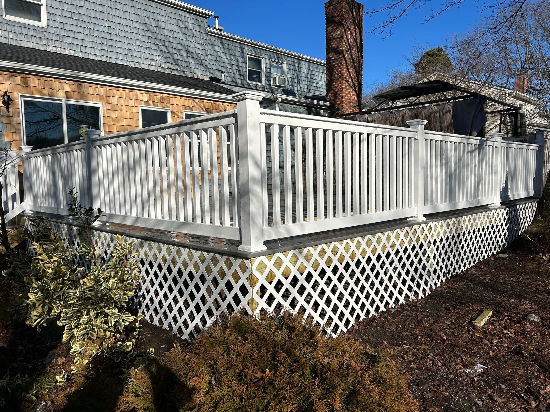 White lattice skirting on a wooden deck with a white railing. Brown brick house in the background.