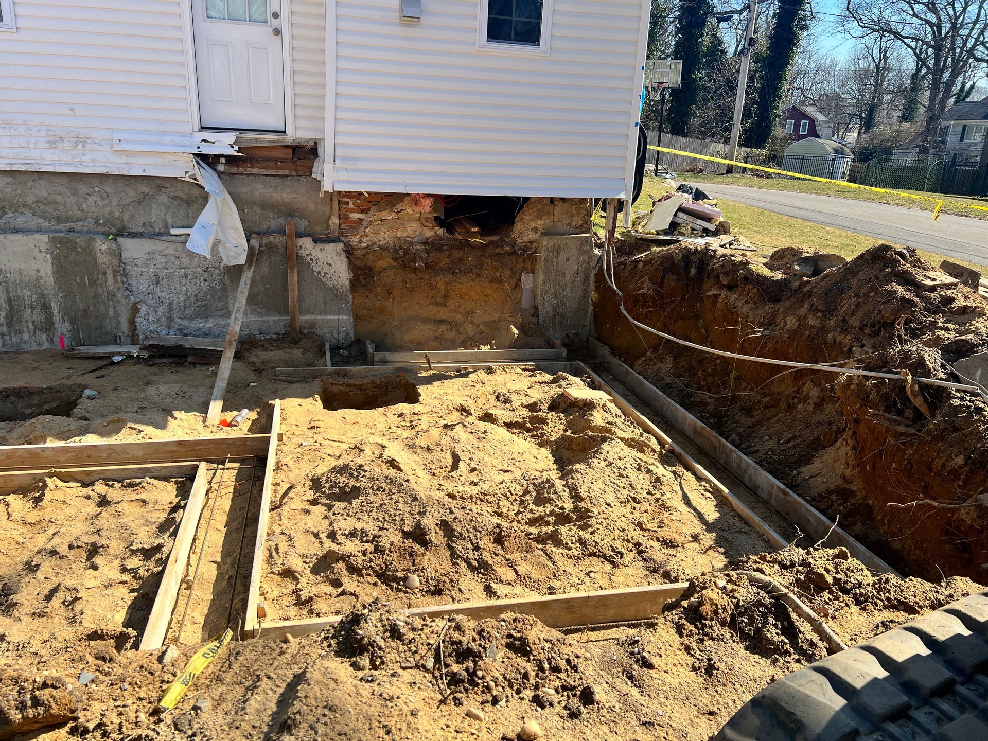 House foundation repair, construction site. Excavated dirt, wood forms, house on concrete base.
