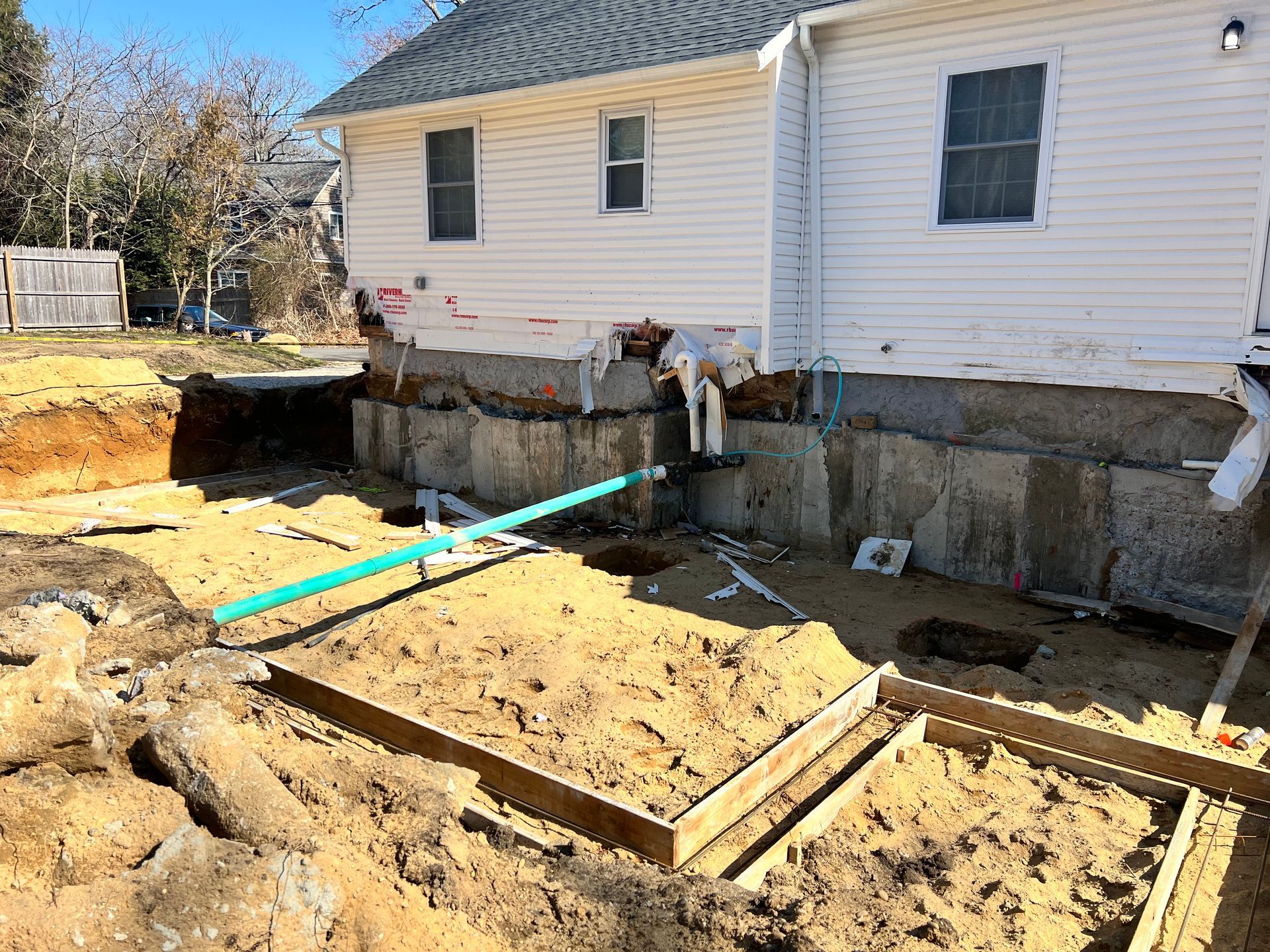 Construction site: House with exposed foundation, trench, and wooden forms.