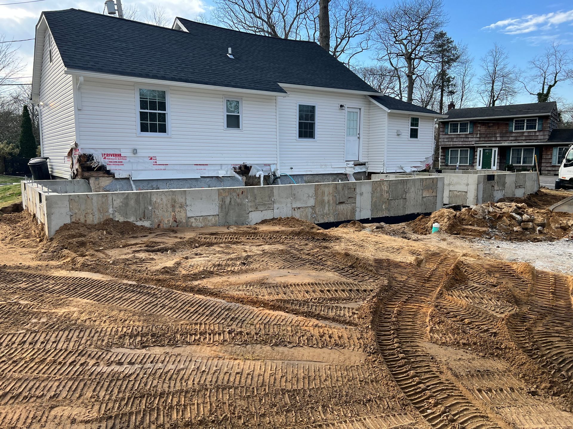 White house on a concrete foundation under construction; dirt and construction debris in foreground.