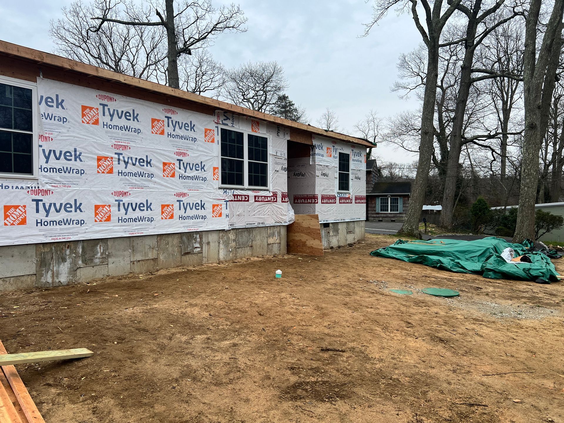 Construction of a house with Tyvek wrap and windows. Exterior shot with dirt and trees.