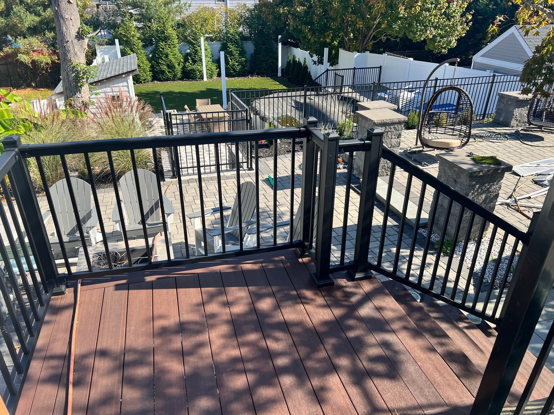 Wooden deck with black railings overlooking a patio with stone and decorative elements.