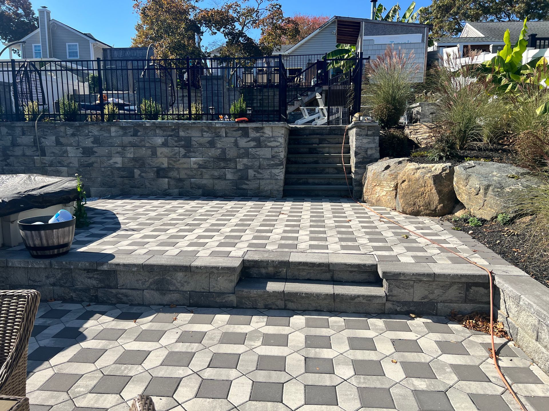 Stone patio with steps and retaining wall, leading to a garden area with a black fence.