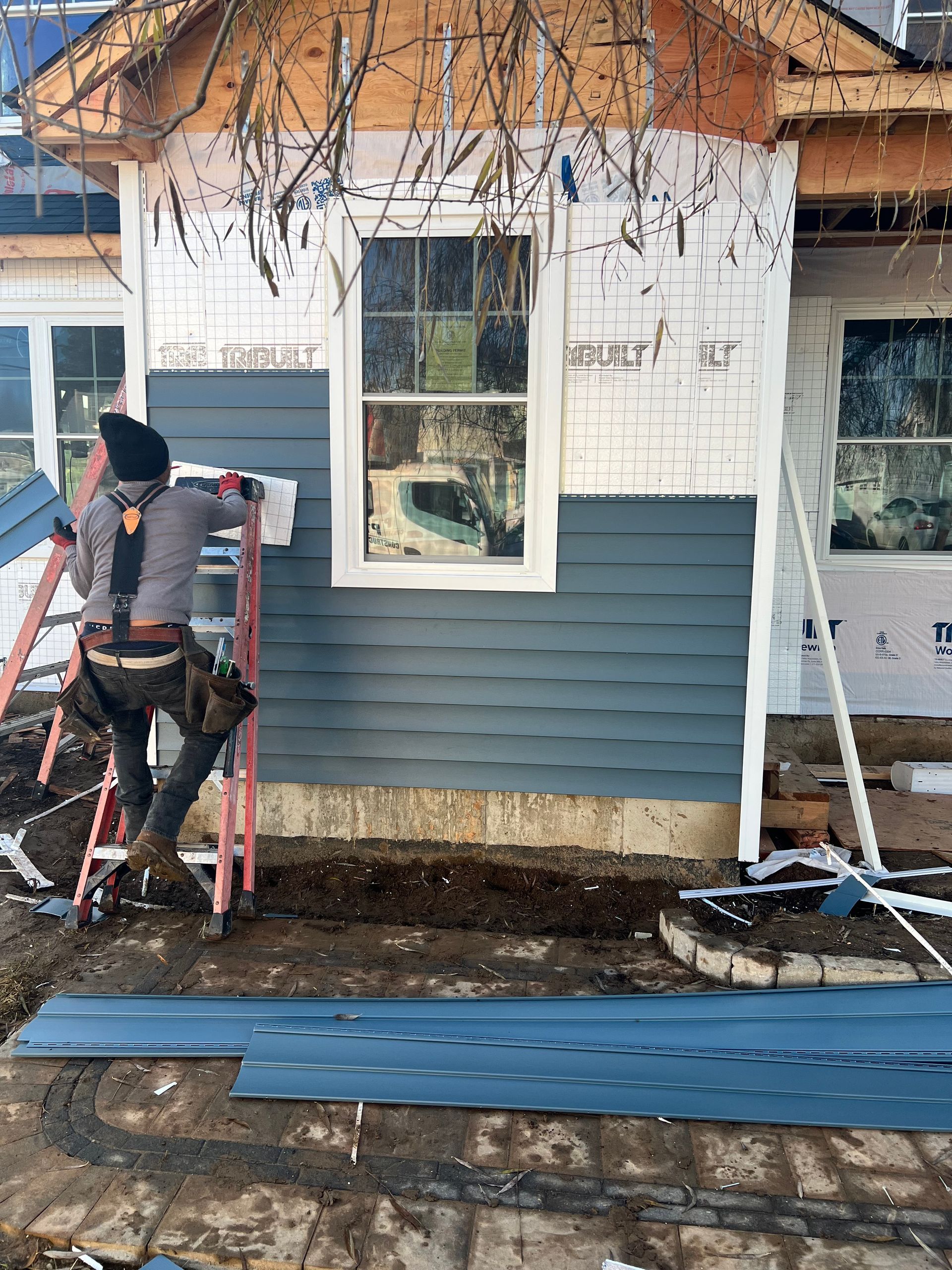 Construction worker installing blue siding on a house exterior.