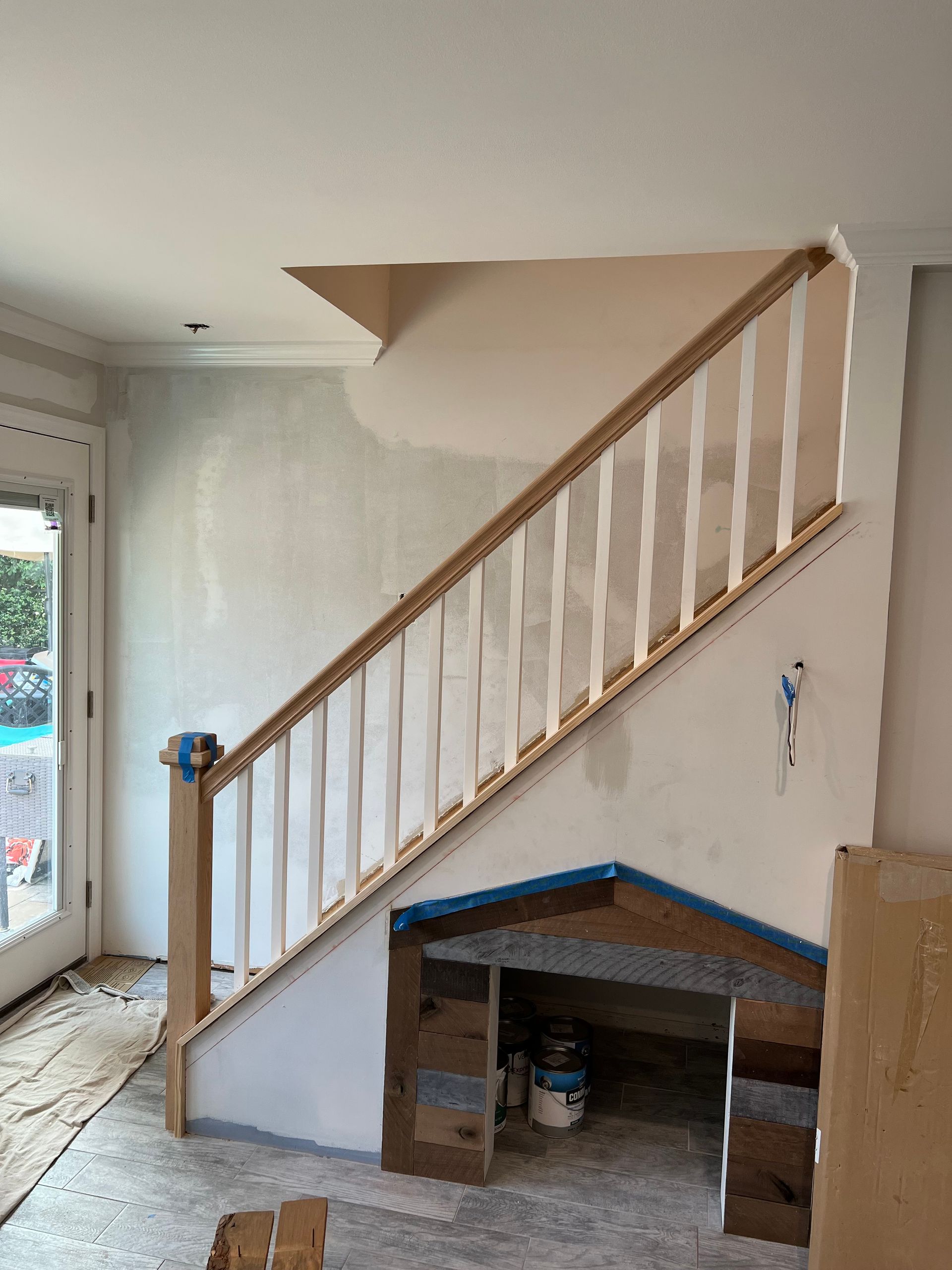 Interior view of a staircase being built. Stair railing and balusters are installed. Paint cans sit inside the unfinished structure.