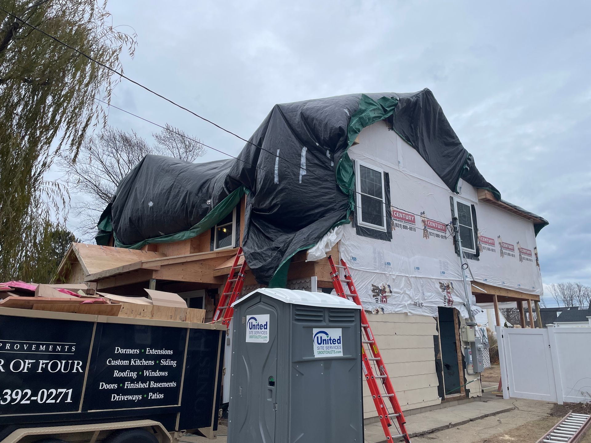House under construction, covered with a tarp, with a portable toilet and debris container in front.