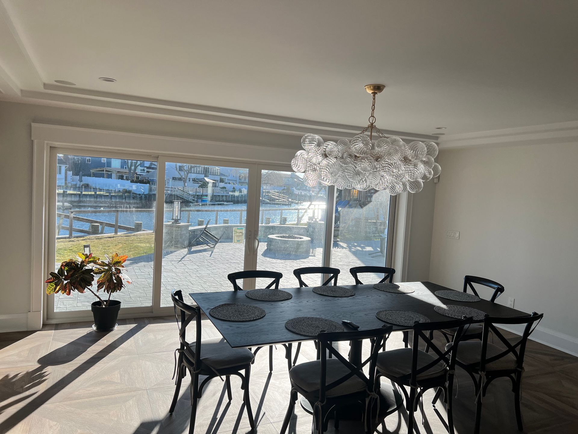 Dining room with a long table, eight black chairs, and large window overlooking a waterside view.