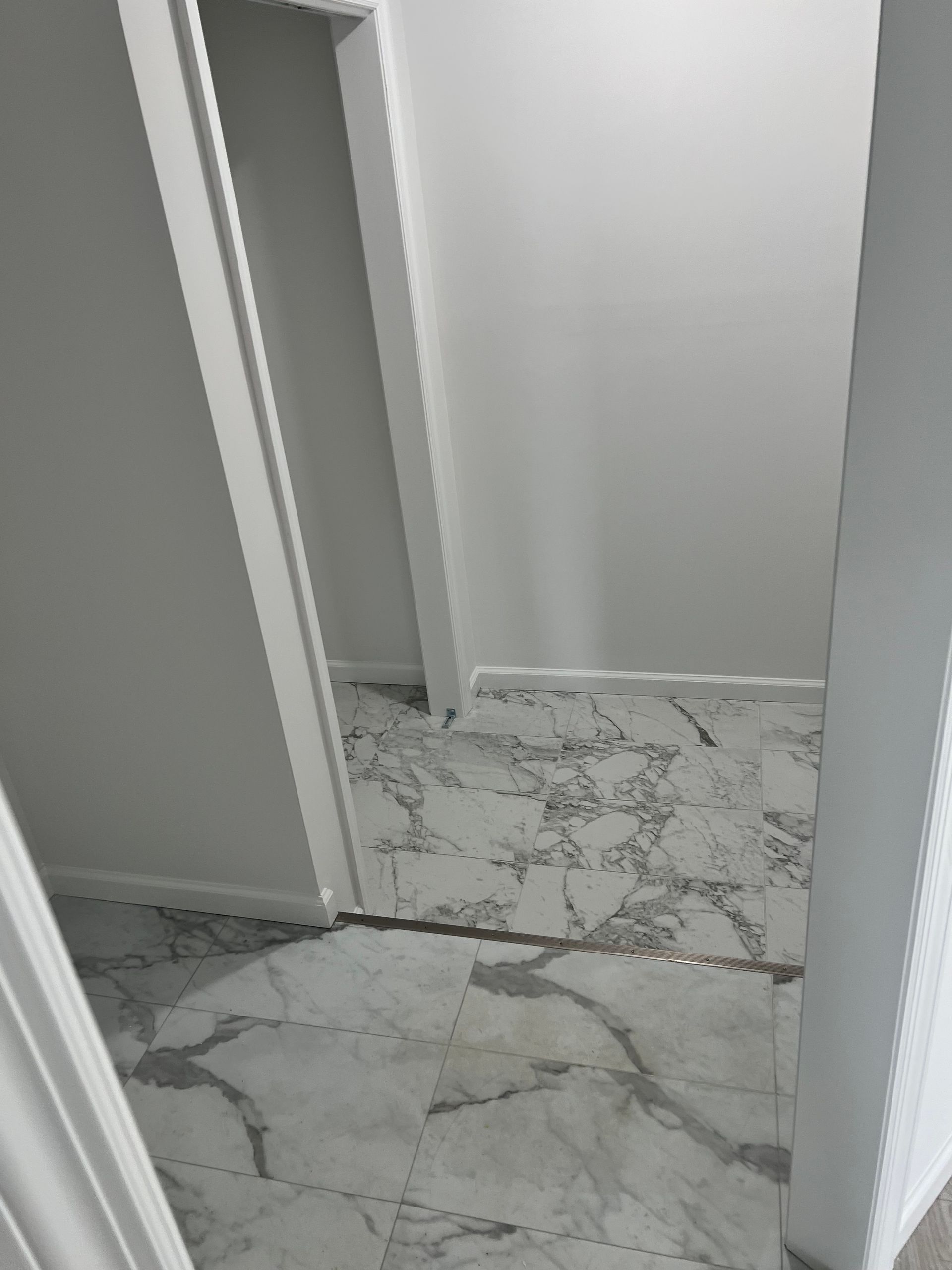 Hallway with white walls and marble-patterned flooring, viewed from a doorway.