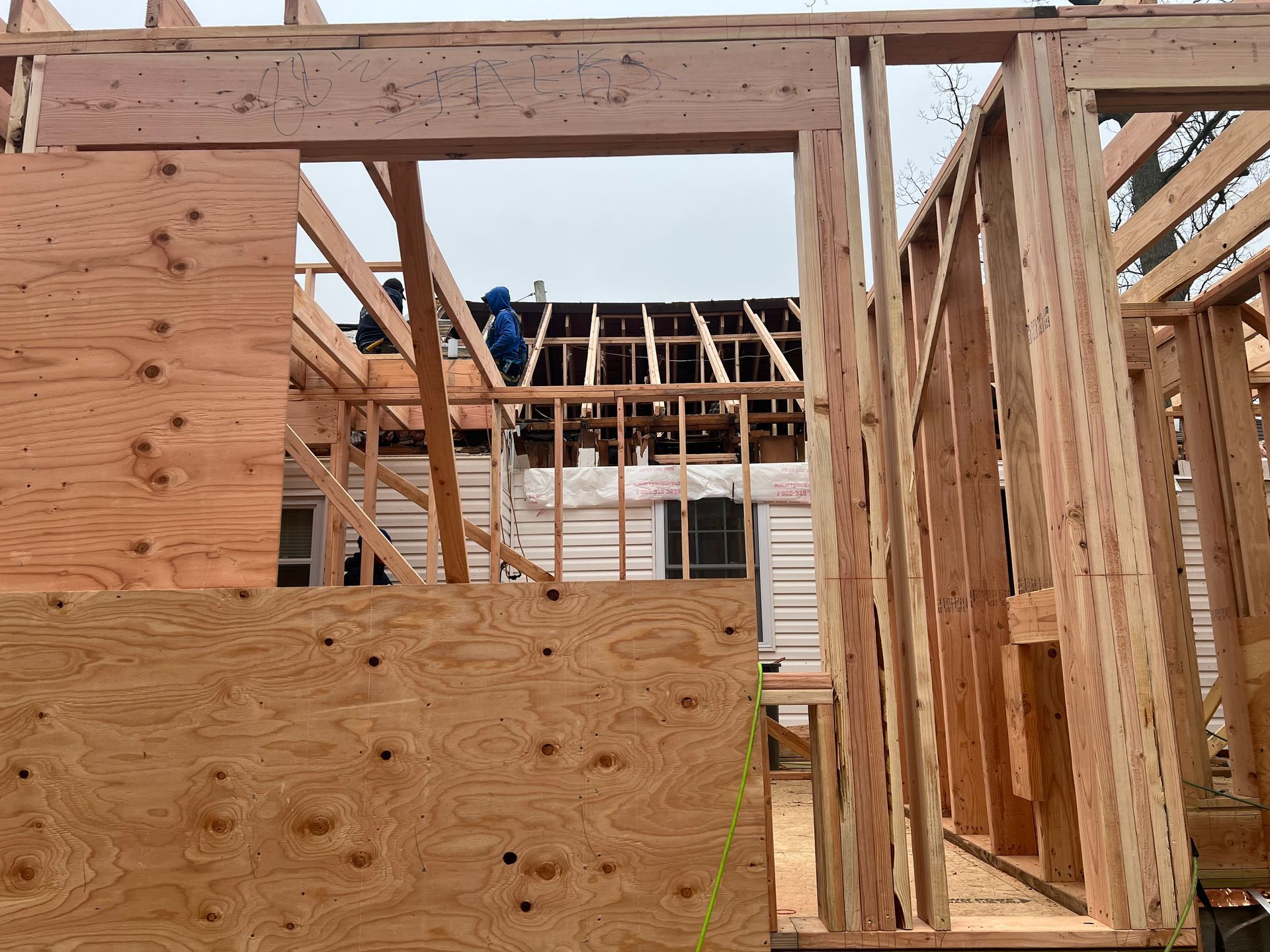 Construction framing of a building with a view of workers on a roof in the background.